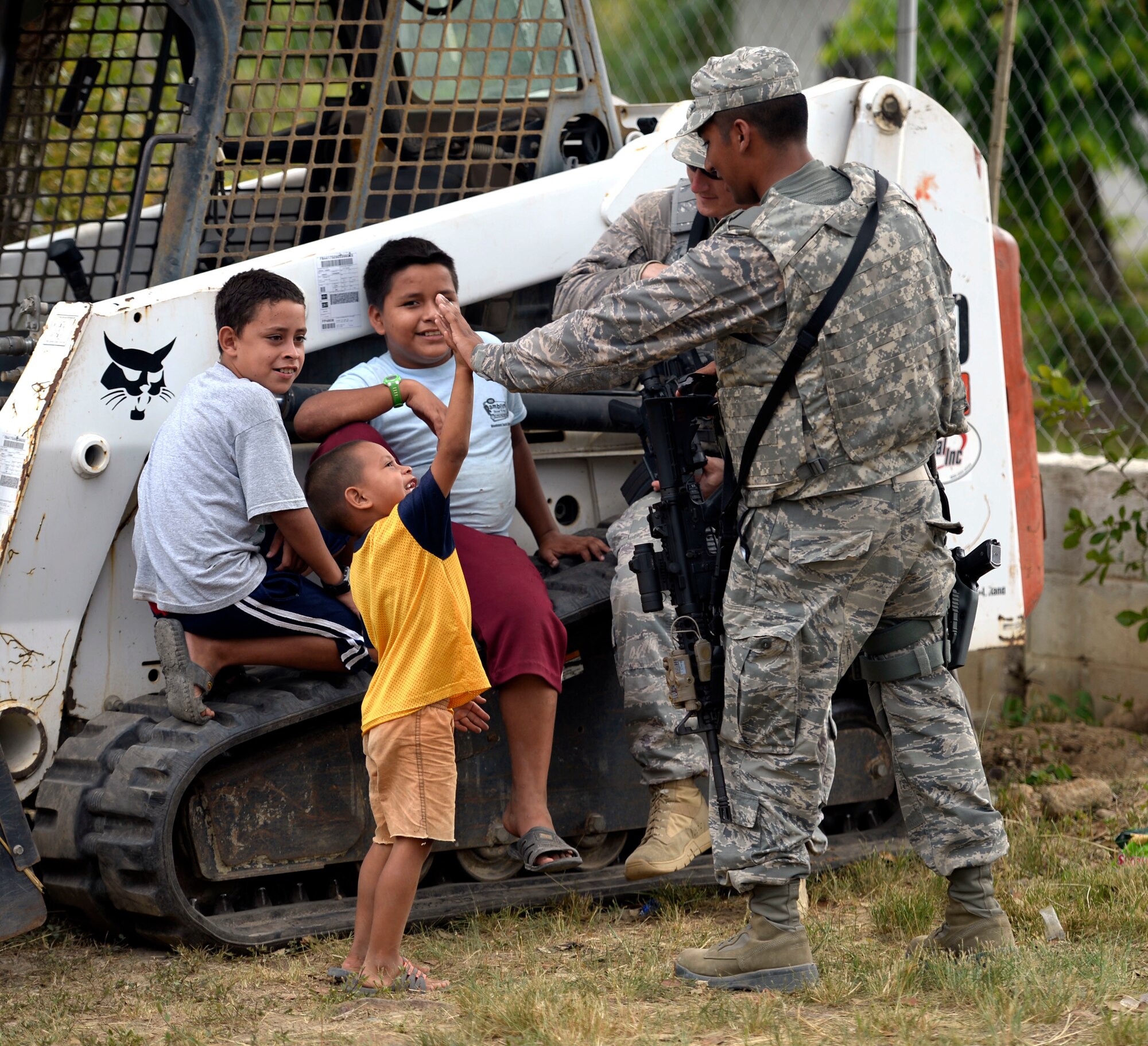 U.S. Air Force Senior Airman Pedro Zambrano, a Dallas, Texas, native with the 301st Security Forces Squadron, out of Carswell, Texas, high fives Christian Trochez, 4, at the Gabriela Mistral primary school construction site in Ocotoes Alto, Honduras, June 1, 2015. Tech. Sgt. Erik Barber, a Arlington, Texas, native with the 610th Security Forces Squadron, also out of Carswell, Texas, hangs out with Osman (center), 13, and Denniz Trochez (left), 10, his cousins. Zambrano and Barber are responsible for security inside the construction site supporting the New Horizons Honduras 2015 training exercise. New Horizons was launched in the 1980s and is an annual joint humanitarian assistance exercise that U.S. Southern Command conducts with a partner nation in Central America, South America or the Caribbean. The exercise improves joint training readiness of U.S. and partner nation civil engineers, medical professionals and support personnel through humanitarian assistance activities. (U.S. Air Force photo by Capt. David J. Murphy/Released)