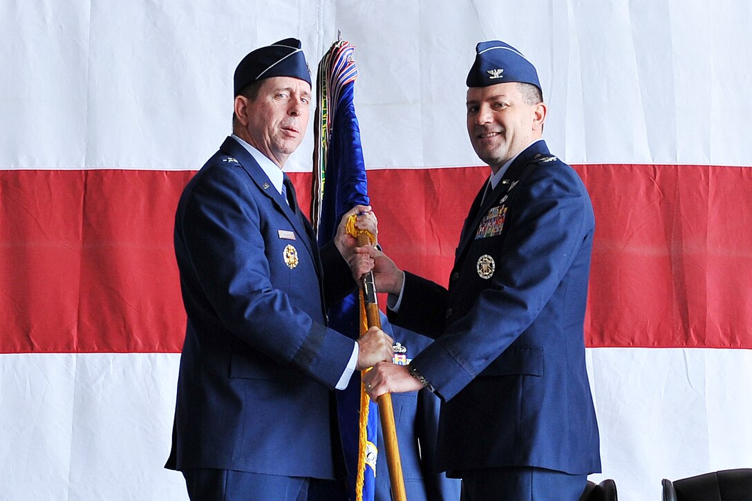 U.S. Air Force Maj. Gen. John N.T. Shanahan, 25th Air Force commander, hands the 55th Wing guidon to U.S. Air Force Col. Marty Reynolds, incoming commander, during the 55th Wing Change of Command inside Dock 1 of the Bennie Davis Maintenance Facility on Offutt AFB, Neb. June 1. As the 55th Wing commander, Reynolds is now responsible for organizing, training, and equipping six groups and 31 squadrons executing worldwide intelligence, surveillance and reconnaissance; electronic attack; command and control; presidential support; and treaty verification missions. He is also responsible for base support to more than 50 associate units, including U.S. Strategic Command, Air Force Weather Agency, and more than 57,000 active-duty members, civilians, family members and retirees. (U.S. Air Force photo by Charles Haymond/Released)