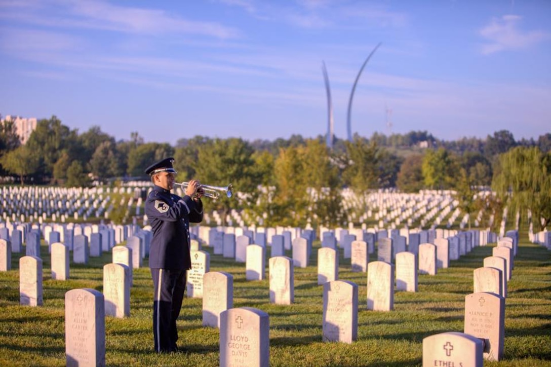 Chief Master Sgt Robert McConnell, a member of the Ceremonial Brass, renders TAPS at Arlington National Cemetery, with the Air Force Memorial visible in the background. (U.S. Air Force Photo by Tech Sgt Matt Shipes/released)