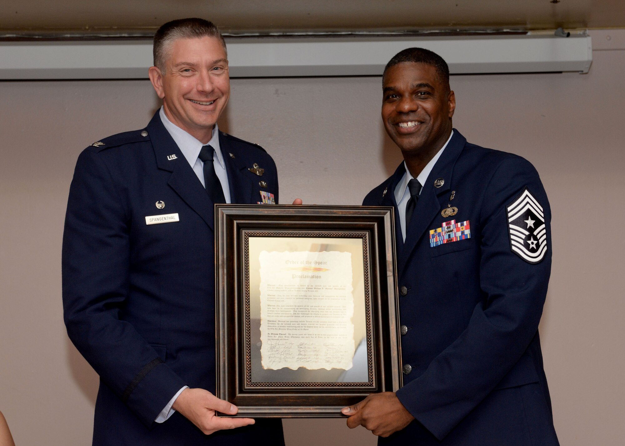 ALTUS AIR FORCE BASE, Okla. – U.S. Air Force Col. Bill Spangenthal, 97th Air Mobility Wing commander, and U.S. Air Force Chief Master Sgt. James Powell, 97th AMW command chief, hold an Order of the Spear Proclamation during a ceremony, June 3, 2015. Spangenthal was inducted into the Order of the Spear which is the highest honor that can be bestowed upon a leader by the enlisted members of the 97th Air Mobility Wing. (U.S. Air Force photo by Senior Airman Franklin R. Ramos/Released)