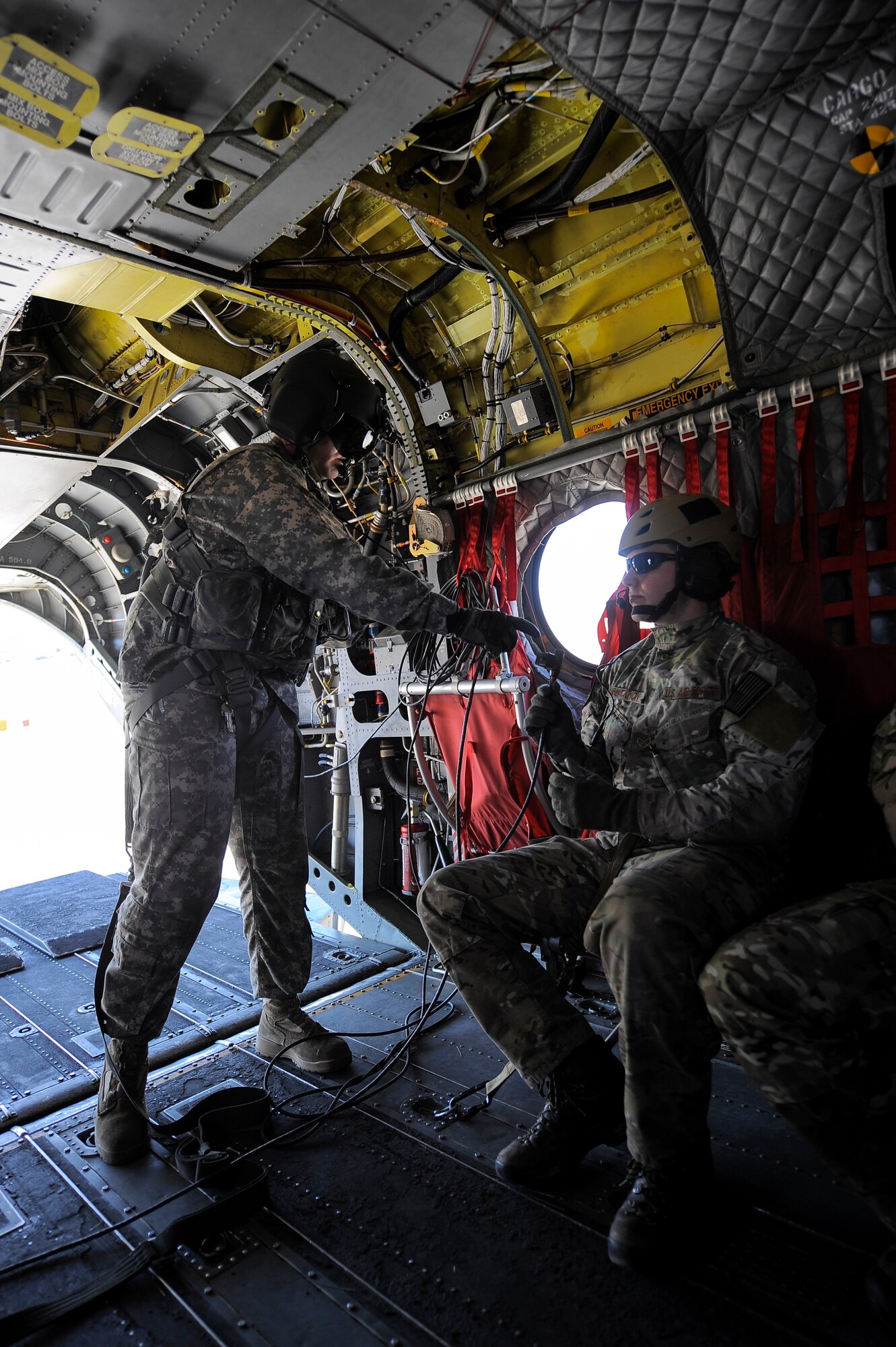 U.S. Army Staff Sgt. Westly Vincent, Task Force Tatanka, CH-47D Chinook flight engineer, hands a headset connector to U.S. Air Force Senior Airman Casey Blackmon 2nd Training Squadron survival, evasion, resistance, and escape specialist, 22nd Training Squadron, Fairchild Air Force Base, Wash., inside a CH-47D Chinook during  Angel Thunder 2015 at Davis-Monthan Air Force Base, Ariz., June 2, 2015. Angel Thunder is the world’s largest personnel recovery exercise, hosting 11 partner nations and nine inter-agencies at Davis-Monthan Air Force Base. (U.S. Air Force photo by Staff Sgt. Angela Ruiz/Released)