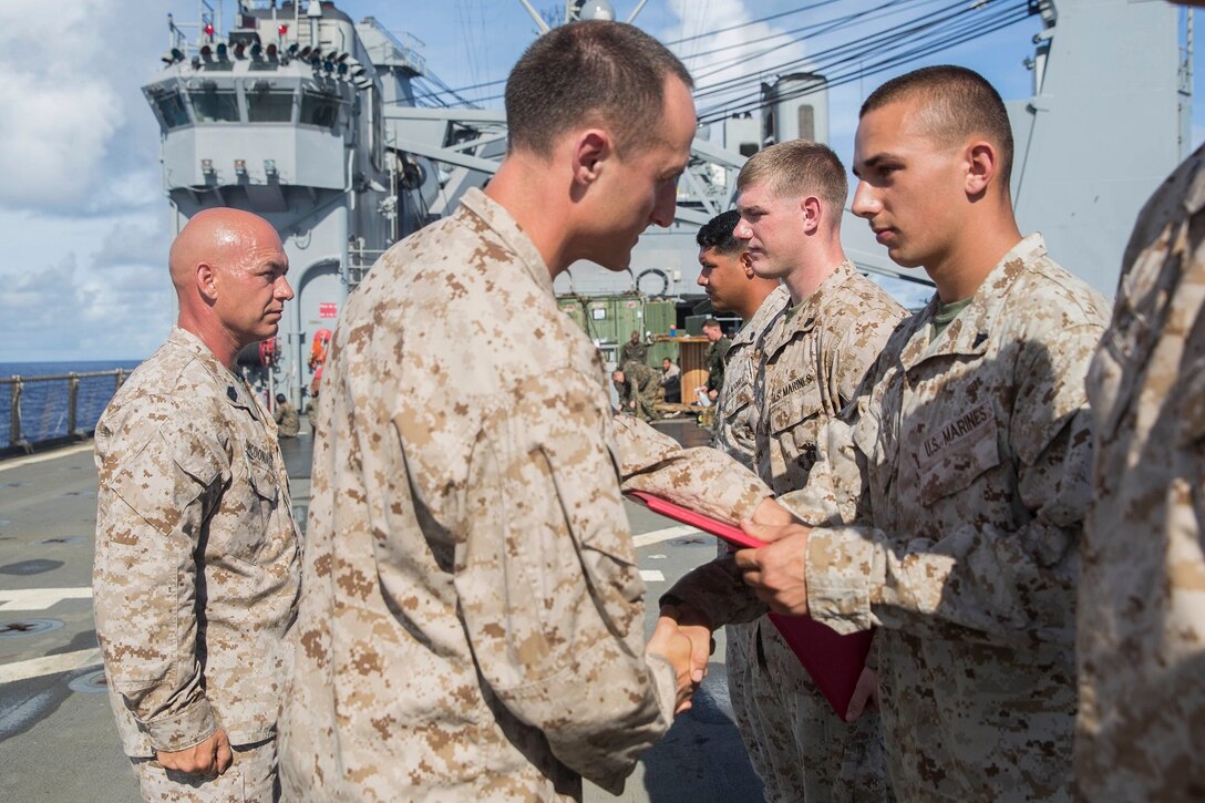 U.S. Marine Capt. Neil MacLaren, middle, congratulates Cpl. Brian Gibson during a promotion ceremony aboard the USS Rushmore (LSD 47) at sea in the Pacific Ocean, June 1, 2015. MacLaren is the commanding officer for Kilo Company, Battalion Landing Team 3rd Battalion, 1st Marine Regiment, 15th Marine Expeditionary Unit. Gibson is an amphibious assault vehicle mechanic with Kilo Co., BLT 3/1, 15th MEU. (U.S. Marine Corps photo by Sgt. Emmanuel Ramos/Released)