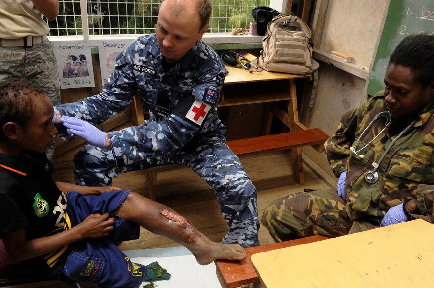 Australian Air Force Squadron Leader Csongor Oltvolgyi, family physician, and Papua New Guinea Defence Force Private Pravate Dulcie Hetewun, medic, examine a local child with an open leg fracture during Pacific Angel 15-4 at Unggai Primary School in Papua New Guinea, June 1, 2015. The medical team treated 514 patients by the end of their first day, and 1,500 more the next two days. The mission of Pacific Angel is to upgrade education and health facilities in the area, as well as work to deepen local disaster response capabilities. (U.S. Air Force photo by Staff Sgt. Marcus Morris/Released)