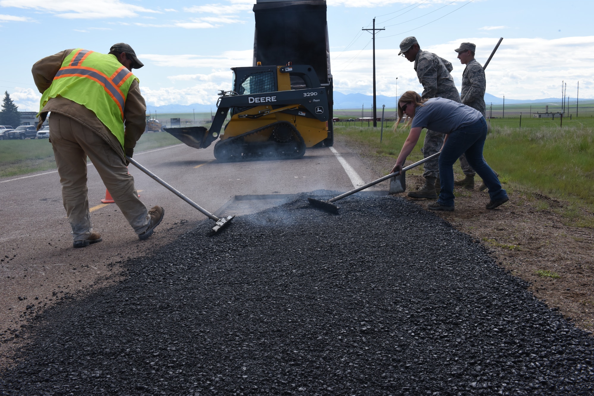 Stephen Links,left, and Senior Airmen Thomas Malloy, Victor Orozco, from the 341st Civil Engineer Squadron pavement and equipment section place hot-mix asphalt to repair defective pavement on Perimeter Road on Malmstrom Air Force Base, Mont., June 3, 2015. Road repair construction maintains 34.6 miles of road, 158.3 acres of paved parking lots, and 13.9 miles of sidewalks. (U.S. Air Force photo/Chris Willis)