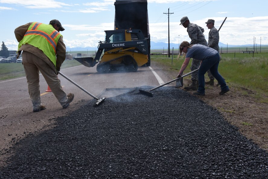 Stephen Links,left, and Senior Airmen Thomas Malloy, Victor Orozco, from the 341st Civil Engineer Squadron pavement and equipment section place hot-mix asphalt to repair defective pavement on Perimeter Road on Malmstrom Air Force Base, Mont., June 3, 2015. Road repair construction maintains 34.6 miles of road, 158.3 acres of paved parking lots, and 13.9 miles of sidewalks. (U.S. Air Force photo/Chris Willis)