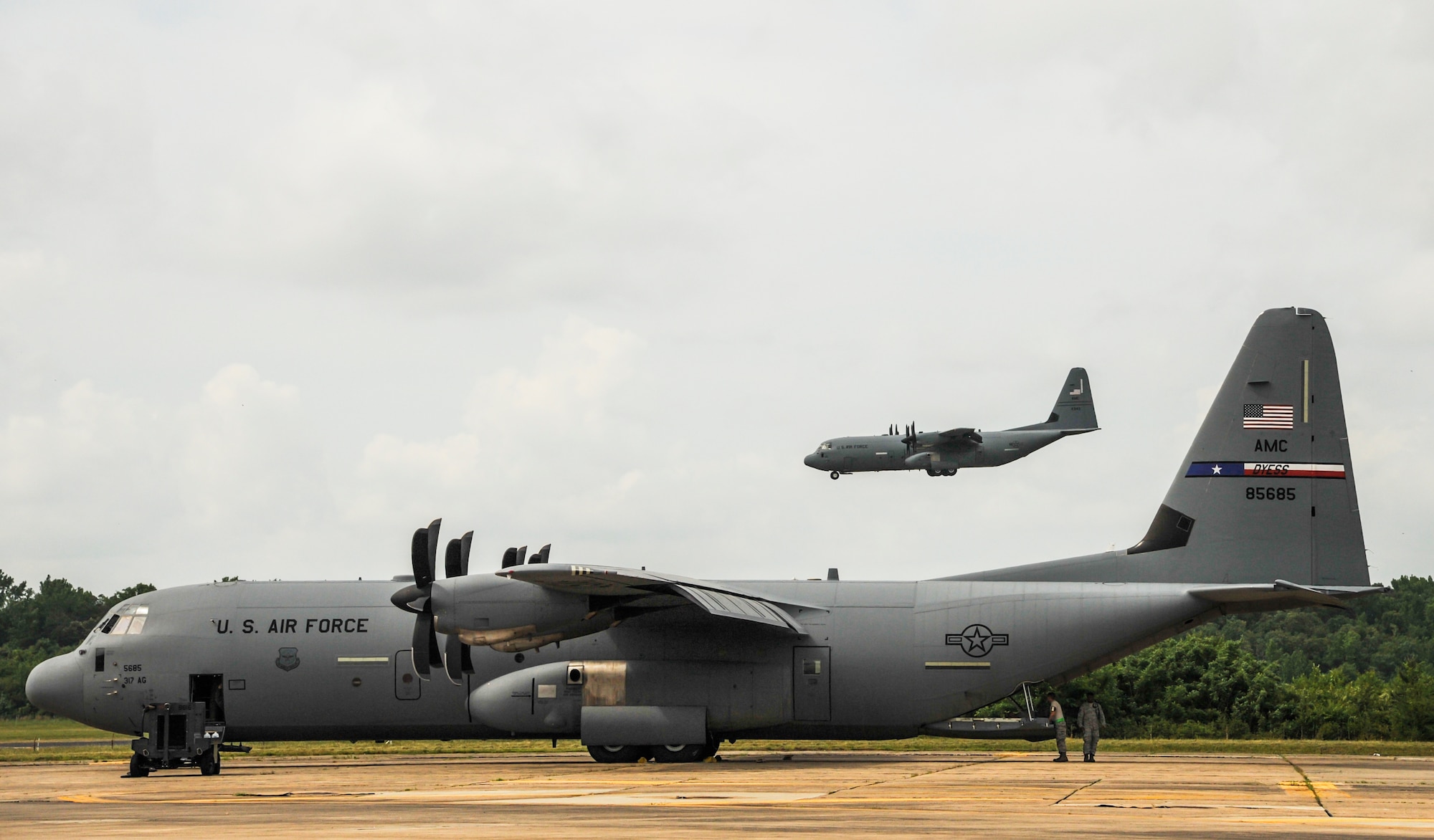 A C-130J prepares to land as a parked C-130J is prepped for departure May 20, 2015, at Little Rock Air Force Base, Ark. The C-130 is one of the most versatile cargo delivery aircraft in the Air Force for its airdrop and air-land mission capabilities (U.S. Air Force photo by Senior Airman Harry Brexel)