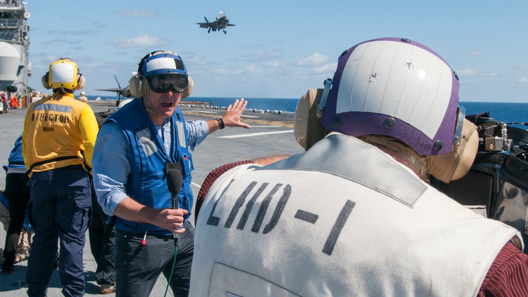 BBC News TV reporter Jonathan Beale reports from the flight deck of USS Wasp while an F-35B Lightning II lands in the background during an F-35B media day. Wasp, with VMFA-121 and VMFAT-501 embarked, is underway conducting the first phase of operational testing for the F-35B aircraft, which will evaluate the full spectrum of F-35B measures of suitability and effectiveness in an at-sea environment.