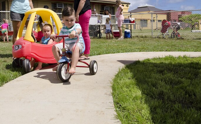 Tyler Roberthon, 2, rides on the new trike path during a mini family fun fair for the Kaneohe Bay Armed Services YMCA in building 455, May 29, 2015. The new trike path and accompanying shade structure were both recently completed and opened to families. The top of the shade structure is blue to represent the ASYMCA and the poles are red to represent the Marine Corps. (U.S. Marine Corps photo by Kristen Wong/Released)