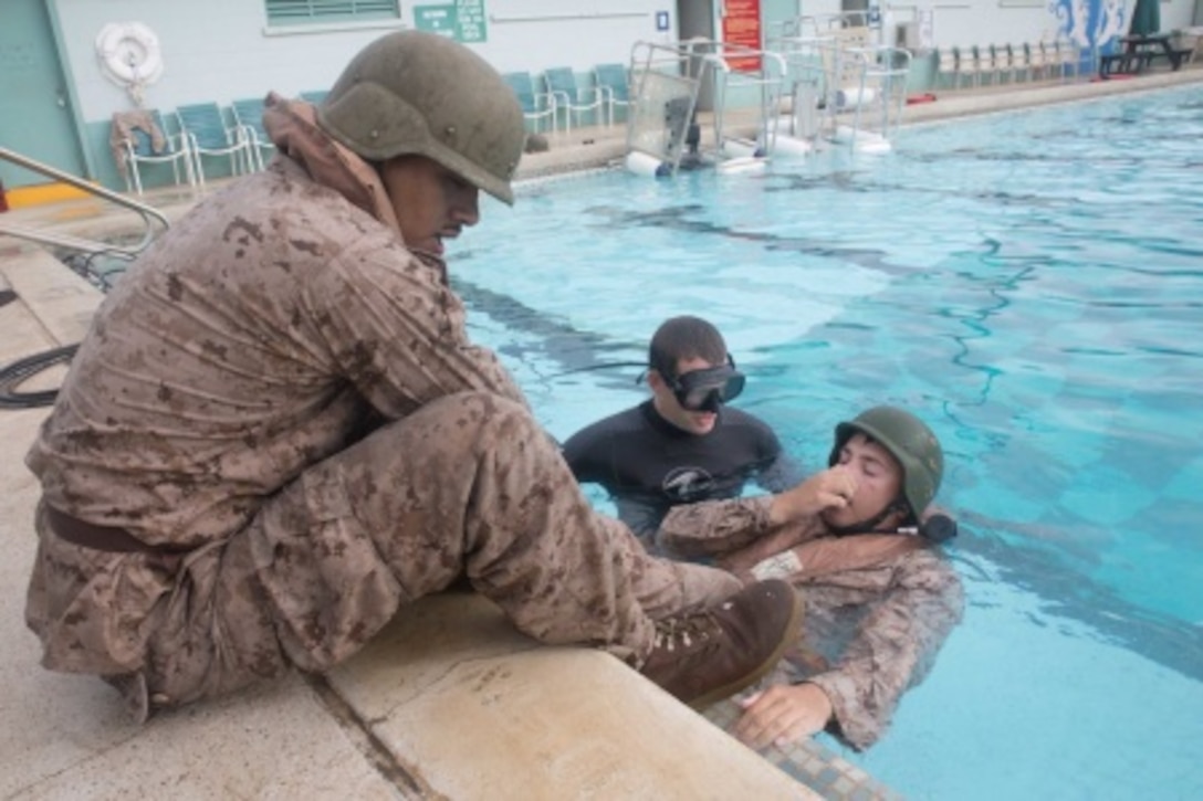 Cpl. Manuel Concreras, a wireman with 2nd Battalion, 3rd Marine Regiment, holds Cpl. Jared Malczewski's legs as he prepares to orient himself upside down in the base pool as a part of Shallow Water Egress Training June 3, 2015 at the base pool aboard marine Corps Base Hawaii. In this scenario, the Marines learned how to don their oxygen apparatus while underwater.