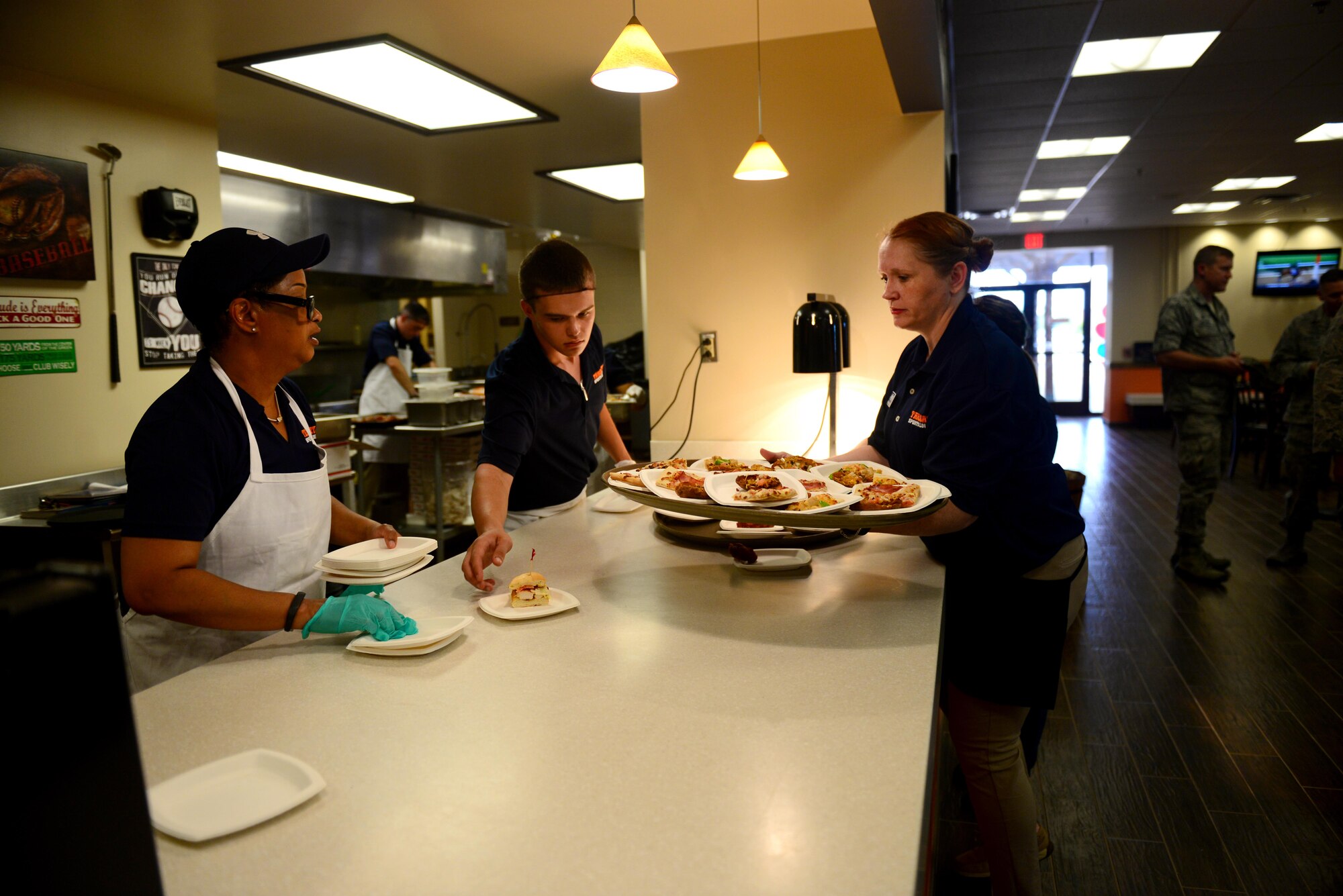 Terese Harris, 27th Special Operations Force Support Squadron deputy, and Airman 1st Class Zakary West, 27th SOFSS food apprentice, pass food samples to Senior Master Sgt. Jennifer Holton, 27th SOFSS military personnel flight superintendent, June 4, 2015 at Cannon Air Force Base, N.M. Free samples of the Tailgate Sports Lounge’s new menu were offered at the Drop Zone’s reopening. (U.S. Air Force Photo/Airman 1st Class Shelby Kay-Fantozzi)