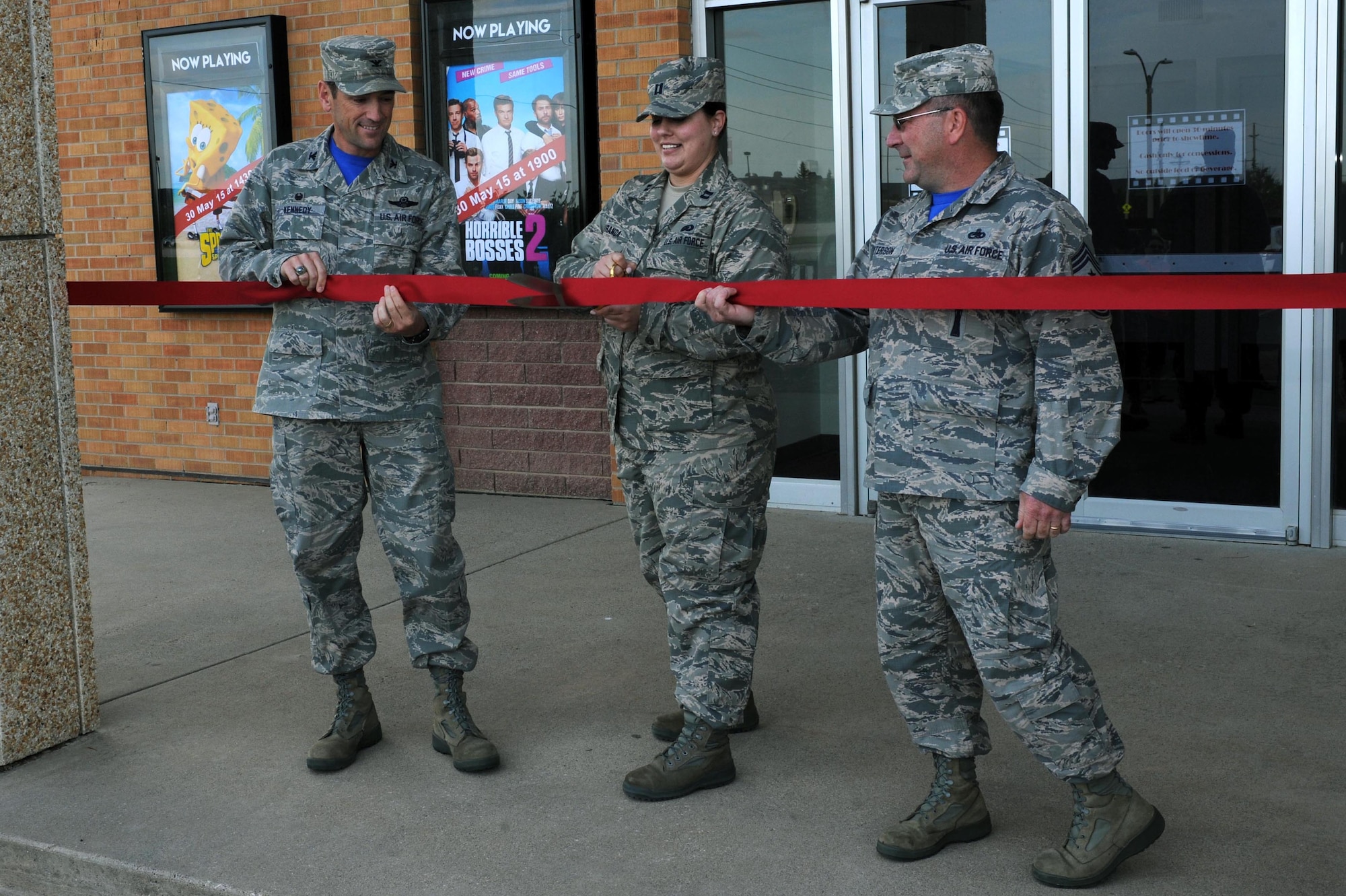 Col. Kevin Kennedy (left), 28th Bomb Wing commander, Capt. Kristen Miranda (middle), 28th Force Support Squadron executive officer, and Chief Master Sgt. Kevin Peterson (right), 28th BW command chief, cut the ribbon at the Base Theater Grand Opening at Ellsworth Air Force Base, S.D., May 29, 2015. The theater shows two free movies each week and sells concessions sponsored by both the 28th FSS and private organizations which can be paid for in cash. (U.S. Air Force photo by Senior Airman Hailey R. Staker/Released)