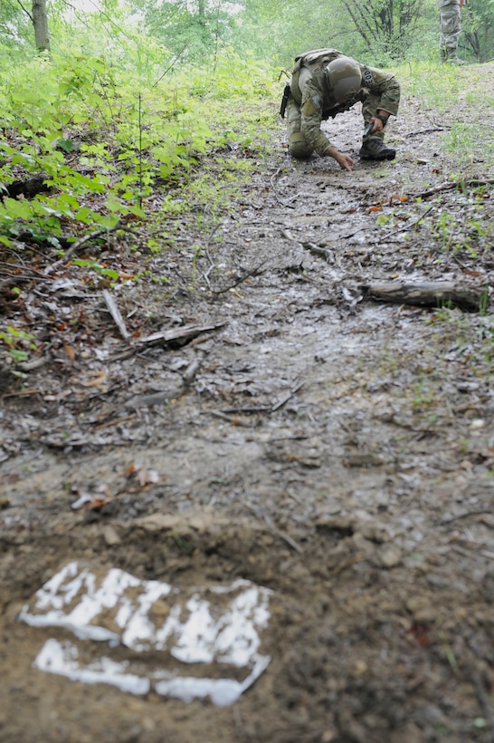 Staff Sgt. Luke Mefford, 11th Civil Engineer Squadron Explosive Ordnance Disposal training and quality control technician, inspects the area around an uncovered training device June 4, 2015, on Joint Base Andrews, Md. Many improvised explosive devices can be set or linked together, so EOD technicians search for additional devices after finding one. (U.S. Air Force photo by Senior Airman Preston Webb/Released)