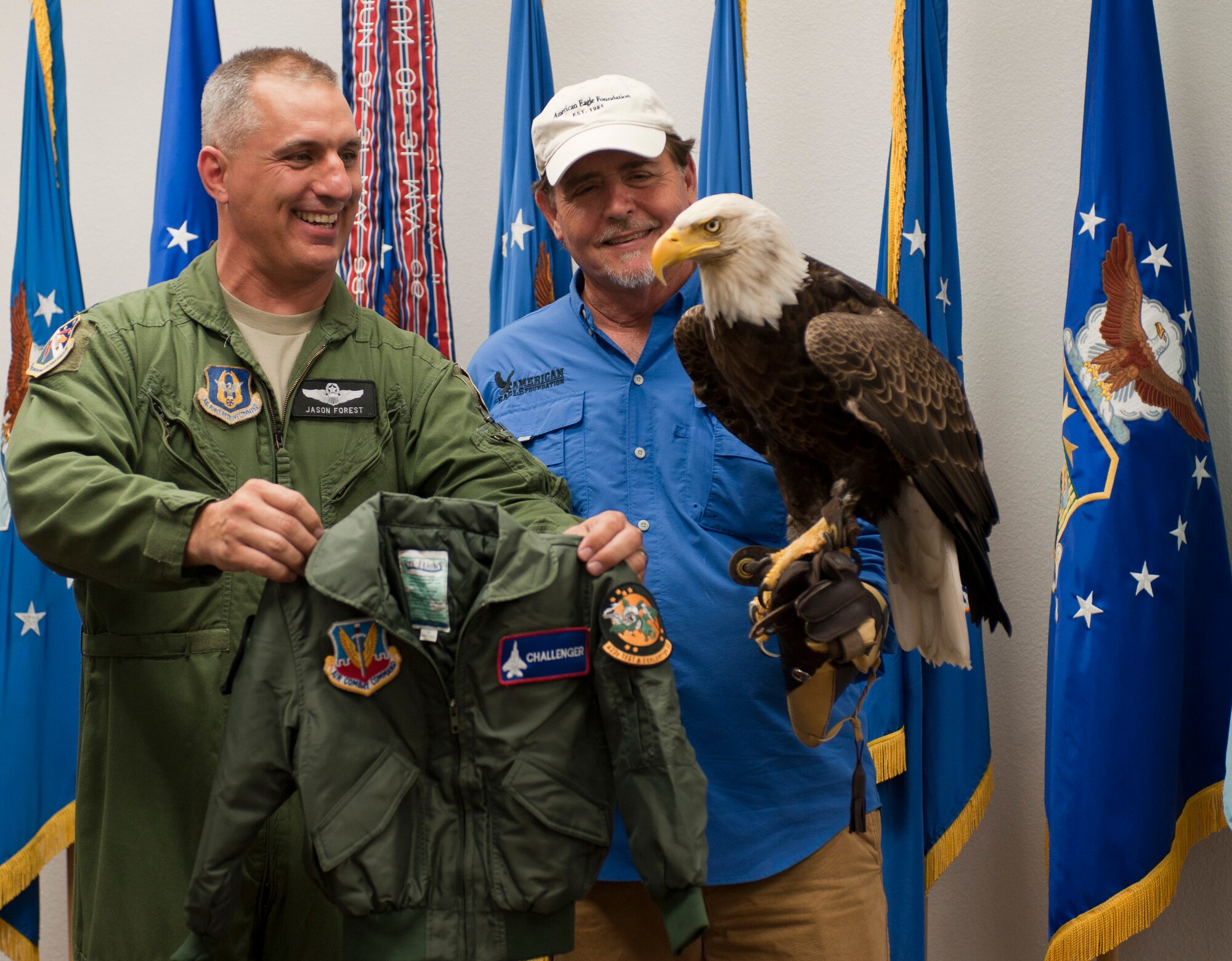 Lt. Col. Jason Forest, 53rd Test and Evaluation Group, presents Al Cecere, founder, president and CEO of the American Eagle Foundation, with a flight suit jacket for Challenger, a bald eagle, at the U.S. Air Force Warfare Center on Nellis Air Force Base, Nev., May 29, 2015. Challenger visited Lomie G. Heard Elementary School, the 757th Aircraft Maintenance Squadron Eagle and Strike Aircraft Maintenance Units, and the U.S. Air Force Warfare Center. (U.S. Air Force photo by Airman 1st Class Mikaley Towle)