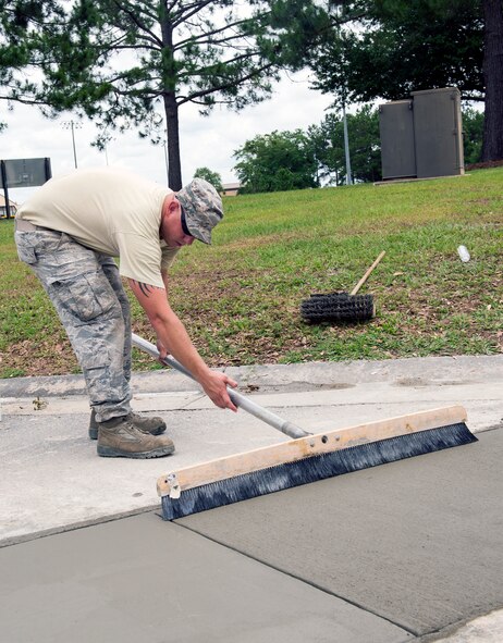 U.S. Air Force Staff Sgt. Travis Woody, 23d Civil Engineer Squadron heavy equipment operator, sweeps over drying pavement during a road repair June 2, 2015, at Moody Air Force Base, Ga. Woody swept the pavement for a smooth finish signifying completion of the project. (U.S. Air Force photo by Airman Greg Nash/Released
