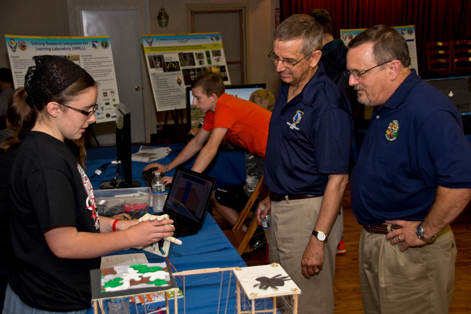 Tashayla Benedict, a 9th grader from the Tri-Village School District, demonstrates her animatronic hand to Dr. David Luginbuhl, (Assistant Chief Scientist/711 HPW) and Dr. Winston "Wink" Bennett (Acting, Division Chief/Warfighter Readiness Research Division),  at the 3rd Annual Full Throttle STEM event sponsored by the 711 Human Performance Wing at Eldora Speedway May 6, 2015. (U.S. Air Force photo by Rick Eldridge / Released)
