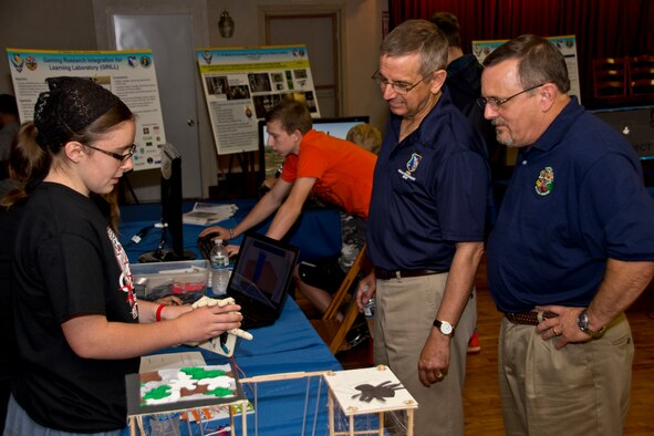 Tashayla Benedict, a 9th grader from the Tri-Village School District, demonstrates her animatronic hand to Dr. David Luginbuhl, Assistant Chief Scientist with the 711 HPW and Dr. Winston "Wink" Bennett, Acting Division Chief, Warfighter Readiness Research Division,  at the 3rd Annual Full Throttle STEM event sponsored by the 711 Human Performance Wing at Eldora Speedway May 6, 2015. (U.S. Air Force photo by Rick Eldridge / Released)
