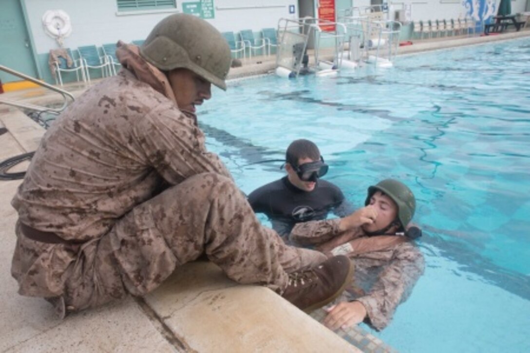 Cpl. Manuel Concreras, a wireman with 2nd Battalion, 3rd Marine Regiment, holds Cpl. Jared Malczewski's legs as he prepares to orient himself upside down in the base pool as a part of Shallow Water Egress Training June 3, 2015 at the base pool aboard marine Corps Base Hawaii. In this scenario, the Marines learned how to don their oxygen apparatus while underwater.