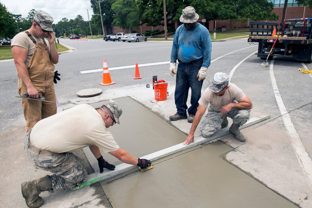 U.S. Air Force Airman 1st Class Adam Backus, 23d Civil Engineer Squadron heavy equipment operator, bottom left, levels the concrete with a middle jointer during a road repair June 2, 2015, at Moody Air Force Base, Ga. Backus aligned the concrete before it hardened to prevent cracking in the concrete. (U.S. Air Force photo by Airman Greg Nash/Released) 