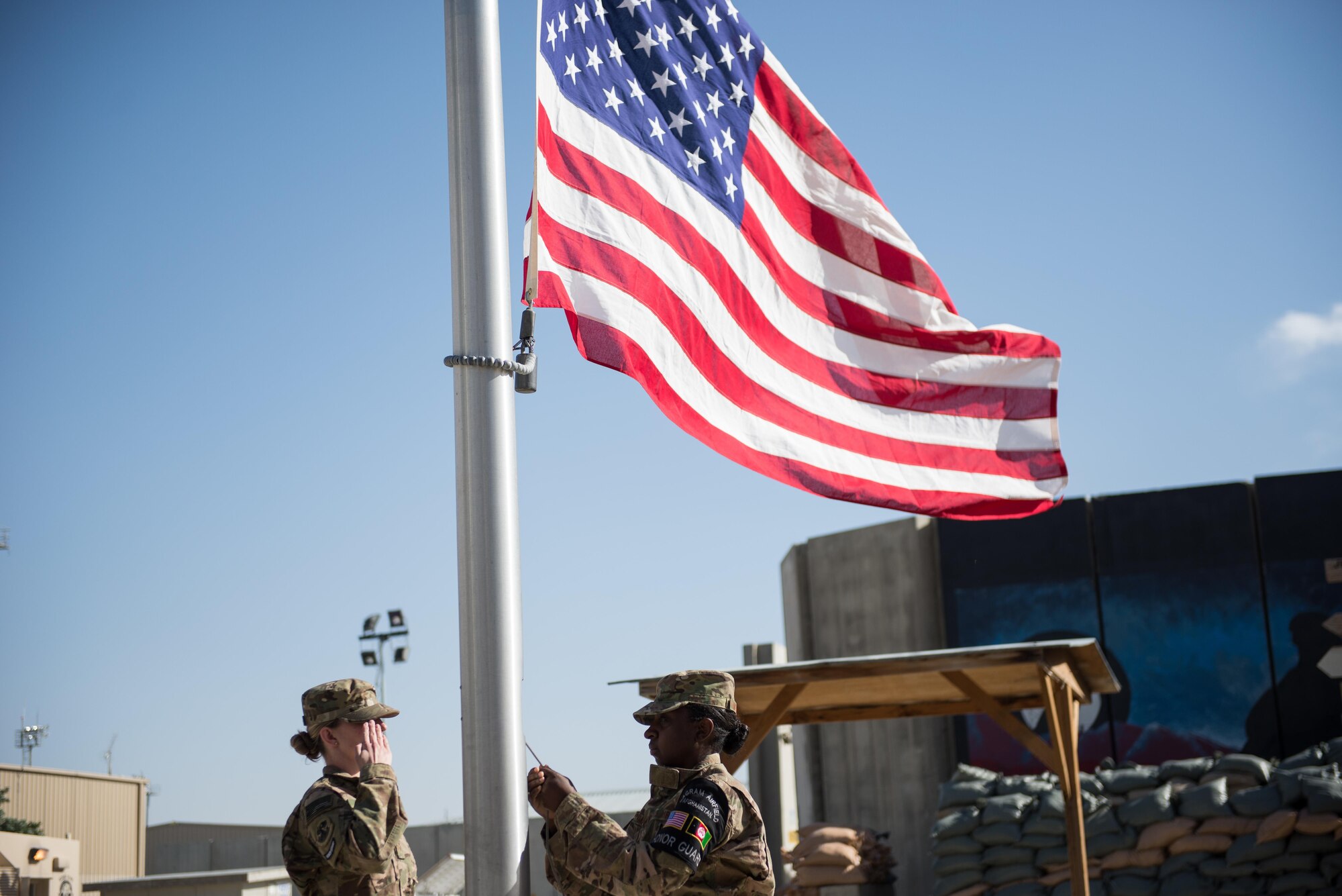 U.S. Air Force Staff Sgt. Anna Melhado and Senior Airman Chelsea Shields, members of the Bagram Air Field Honor Guard, lower the flag during a Memorial Day retreat ceremony at Bagram Air Field, Afghanistan, May 25, 2015. Memorial Day is dedicated to remembering U.S. men and women who gave their lives while in military service protecting and defending national interests. (U.S. Air Force photo by Tech. Sgt. Joseph Swafford/Released)