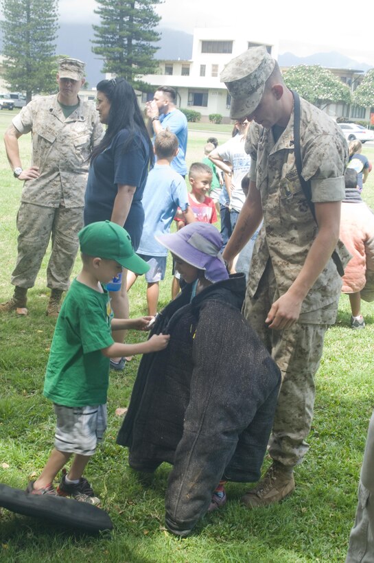 Cpl. Michael Foster, a military working dog handler with the Provost Marshal’s Office helps Kainalu Elementary School students try on a bite suit at Dewey Square, June 2, 2015. Military police officers from PMO showed the dozens of students how the K-9 unit trains dogs for law enforcement. (U.S. Marine Corps photo by Christine Cabalo/Released)