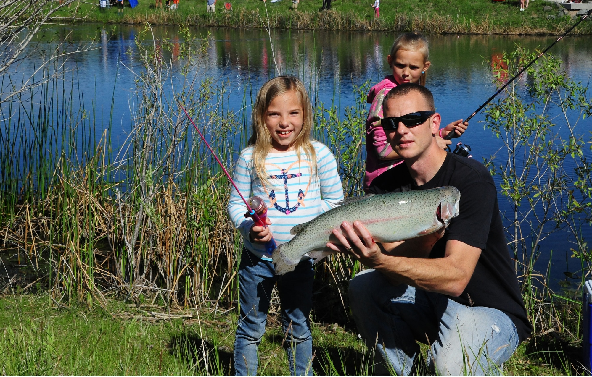 A nearly seven-pound rainbow trout was caught on a pink toy pole by Adalyn Spencer, 6, right, daughter of Krista and Staff Sgt. Adam Spencer, left,  561st Network Operation Squadron mission support analyst. The fish was caught during Kids Fishing Day, Jun. 6, 2015, at Pow Wow Park, Malmstrom Air Force Base, Mont. (U.S. Air Force photo/2nd Lt. Annabel Monroe)
