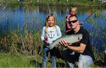 A nearly seven-pound rainbow trout was caught on a pink toy pole by Adalyn Spencer, 6, right, daughter of Krista and Staff Sgt. Adam Spencer, left,  561st Network Operation Squadron mission support analyst. The fish was caught during Kids Fishing Day, Jun. 6, 2015, at Pow Wow Park, Malmstrom Air Force Base, Mont. (U.S. Air Force photo/2nd Lt. Annabel Monroe)