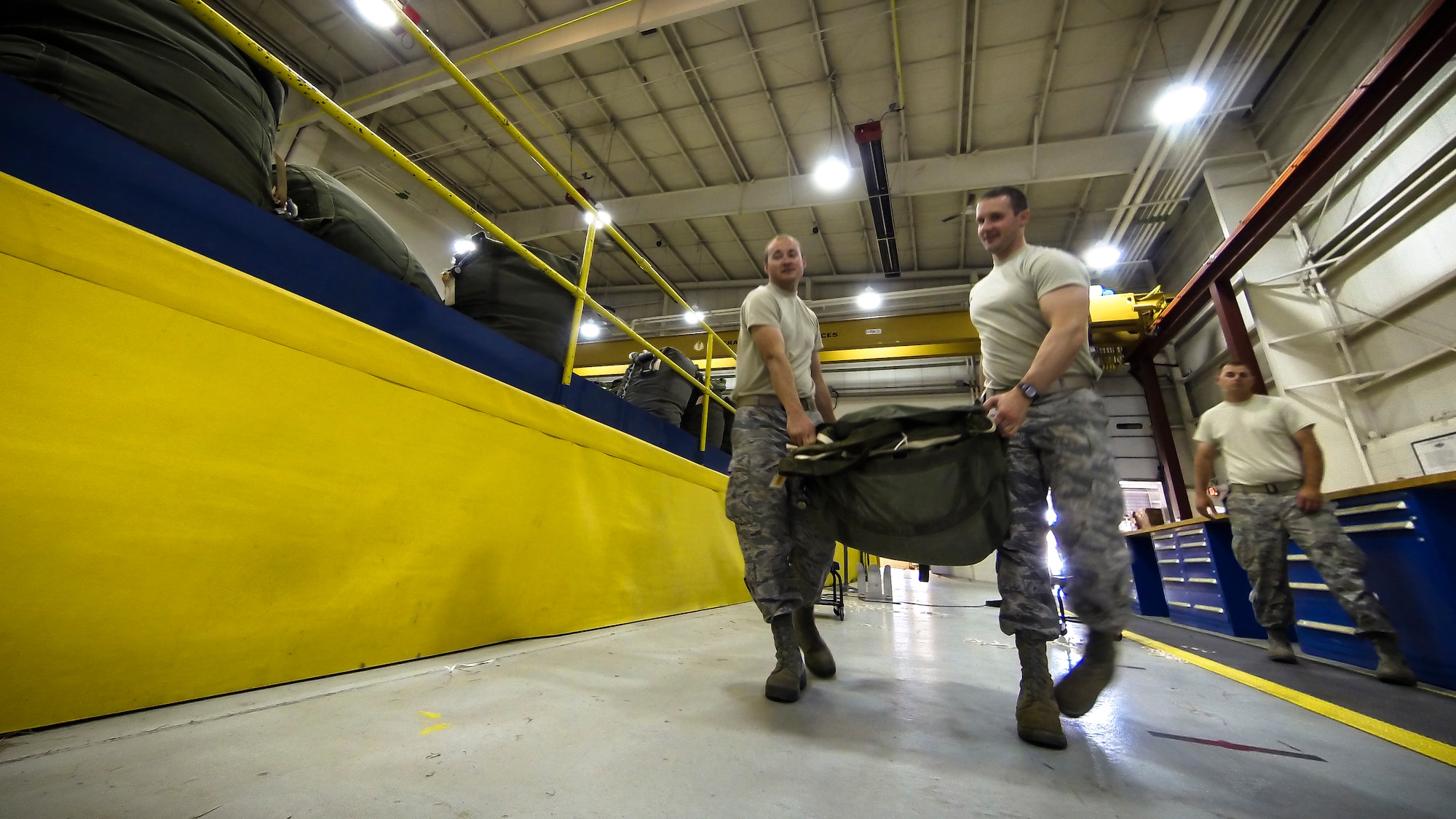 Technical Sgt. Jesse Sorrell (left) and Technical Sgt. Joshua Ellis carry a G-12E Type V platform parachute after recovering it from the dropzone on June 6, 2015 to store it for the next training air drop. The Airman from the 182d Airlift Wing, Small Air Terminal, Peoria, Ill., check and repack the parachute after it was used in a recent C-130 air drop training mission with heavy equipment at the dropzone. (U.S. Air National Guard photo by Master Sgt. Scott Thompson/Released)
