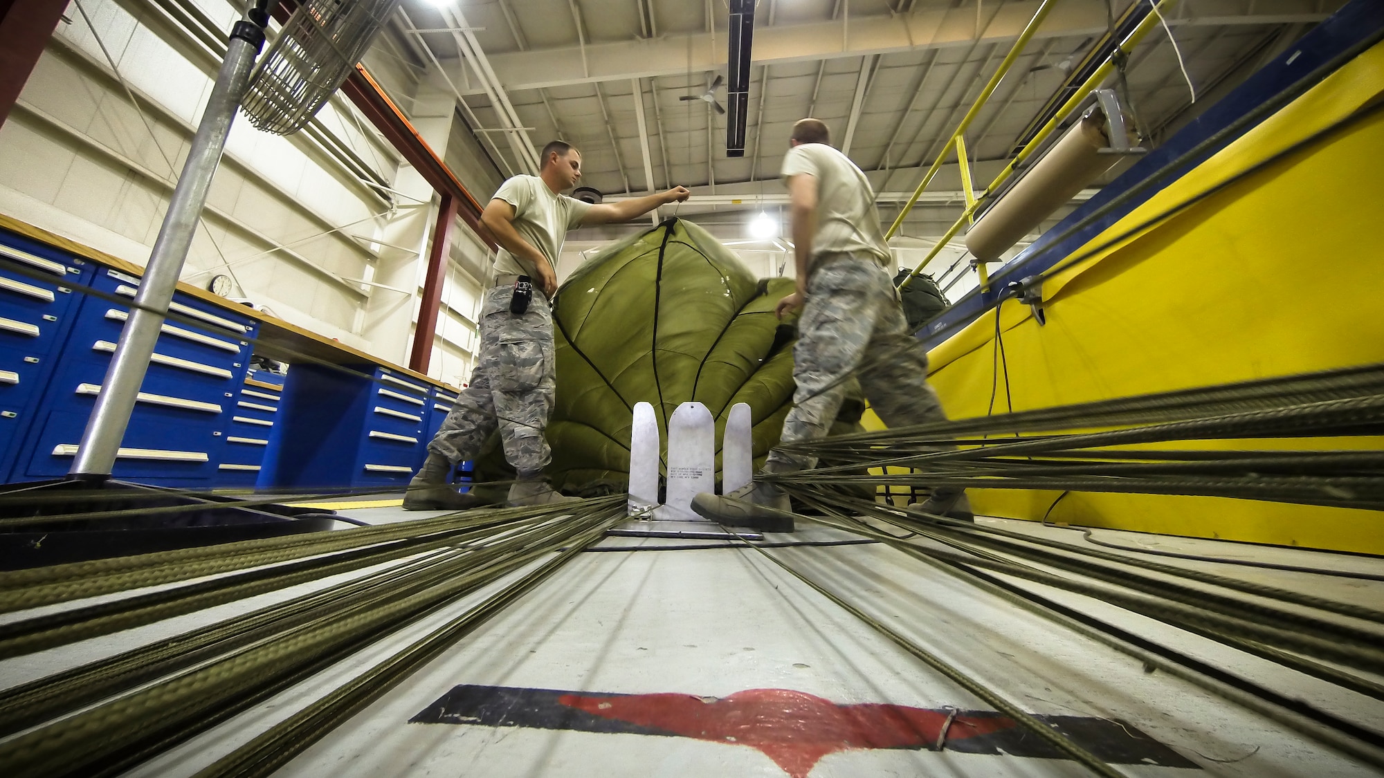 Technical Sgt. Jesse Sorrell (right) and Technical Sgt. Jeremy Martinson (left) untagle parachute cord on a G-12E Type V platform parachute after recovering it from the dropzone on June 6, 2015. The Airman from the 182d Airlift Wing, Small Air Terminal, Peoria, Ill. check and repack the parachute after it was used in a recent C-130 air drop training mission with heavy equipment at the dropzone. (U.S. Air National Guard photo by Master Sgt. Scott Thompson/Released)