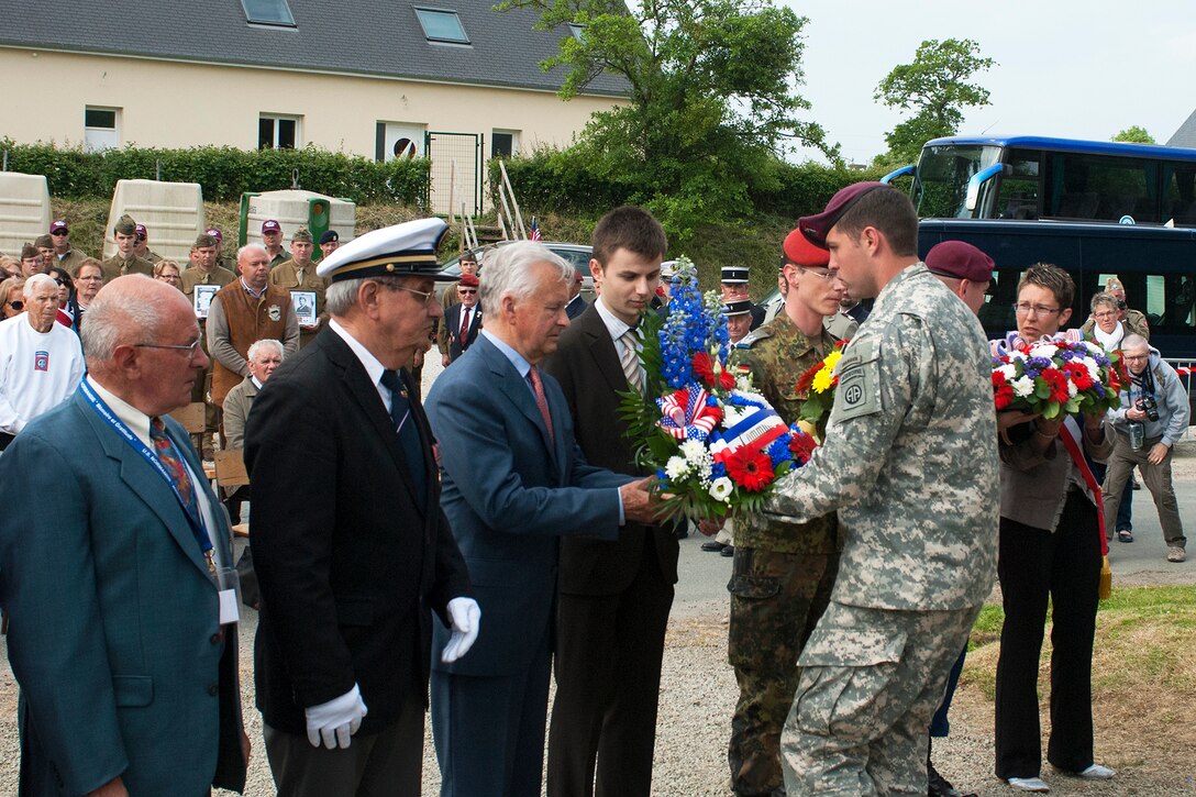 U.S. Army paratrooper Sgt. Tim Carpenter, center right, assigned to 3rd Brigade, 82nd Airborne Division, presents flowers during a ceremony marking the 71st anniversary of D-Day at the Crossroads Memorial site in Gourbesville in the Normandy region of France, June 5, 2015.