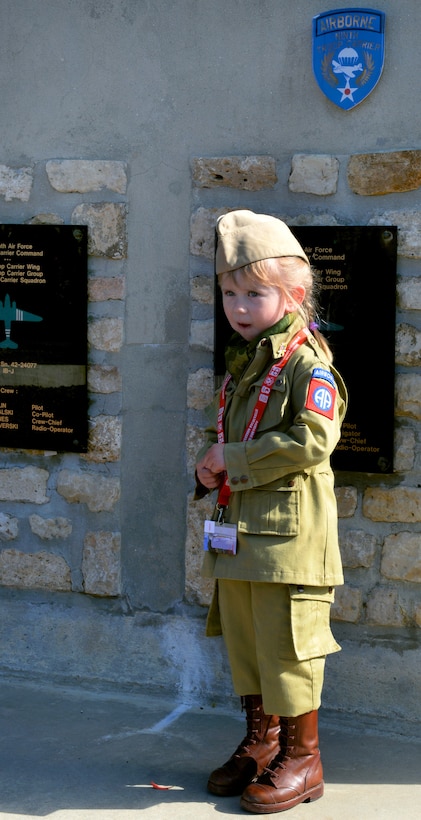 A French girl, dressed in a U.S. Army 82nd Airborne Division vintage World War II uniform, poses in front of a memorial dedicated to U.S. airmen from the 9th Air Force’s Troop Carrier Command and paratroopers from the 82nd and 101st Airborne divisions in Picauville, France. The paratroopers lost their lives when their plane crashed in the town in 1944. 