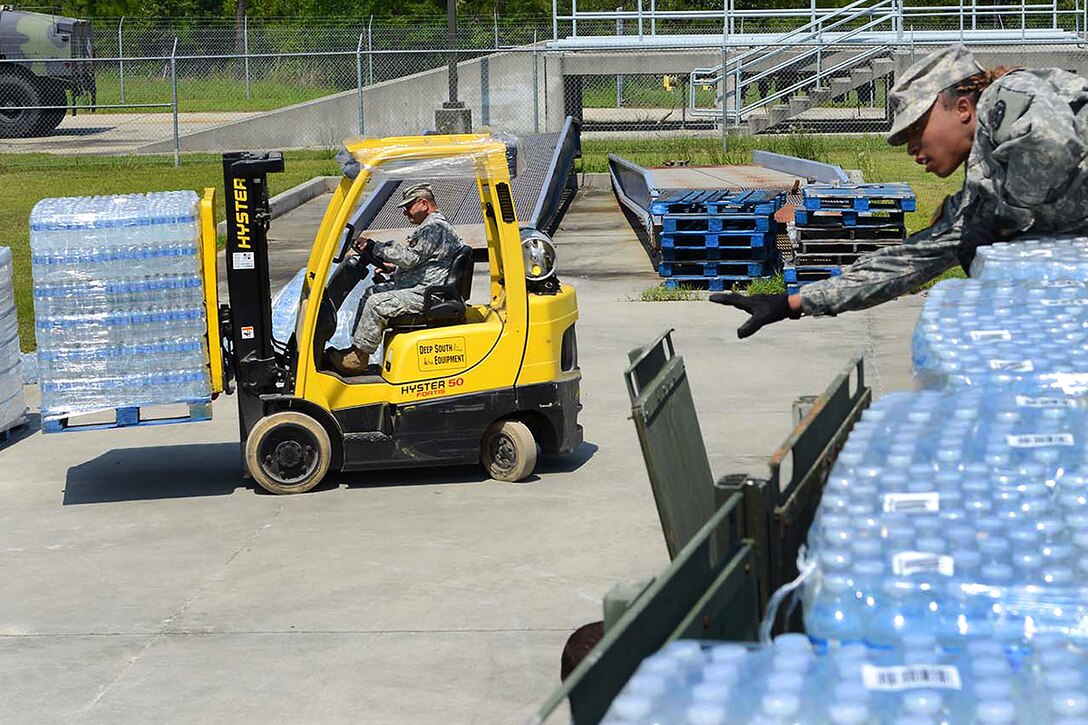 Army Sgt. Denise Sonnier, right, reaches for a sidewall to secure a trailer full of water bottles while retired Army Sgt. Maj. James Serio stages pallets of water bottles on Camp Villere in Slidell, La., June 5, 2015. Sonnier is a motor transport operator assigned to the Louisiana National Guard's 1084th Transportation Company and Serio is a warehouse manager assigned to the Louisiana State Guard. The guardsmen are transporting water and other supplies to Northwest Louisiana to respond to flooding along the Red River.