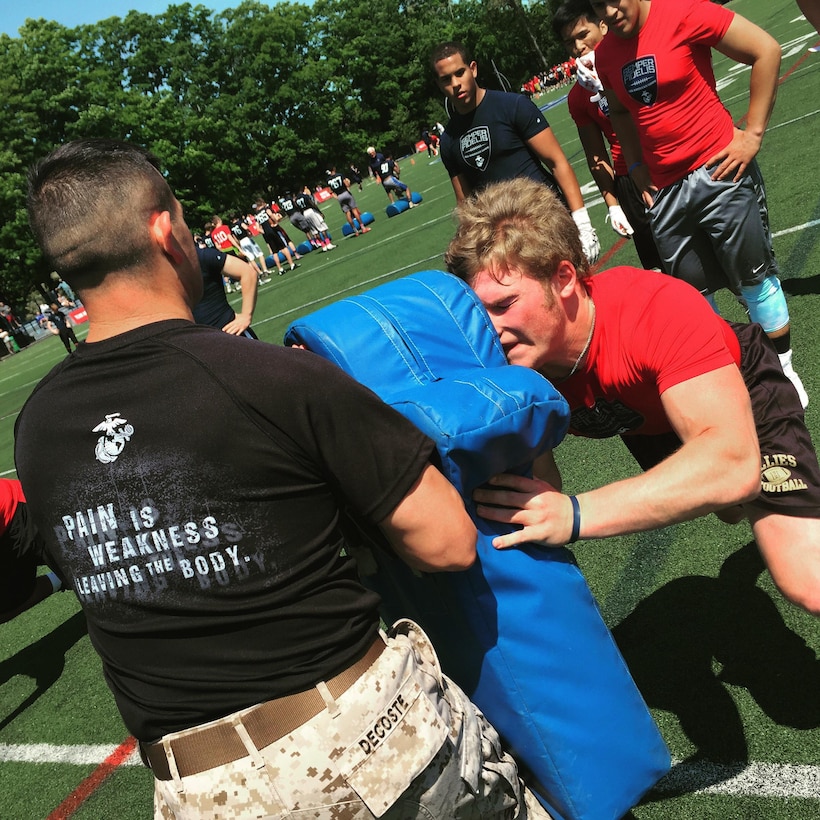 Sergeant Paul Decoste holds a body pad as high school football players rehearse offensive drills during the Semper Fidelis All-American Camp at St. John Preparatory High School in Danvers, Massachusetts, June 7. Nearly 200 top football players from high schools throughout the New England states, including New York, Pennsylvania and New Jersey, received training from National Football League and college football coaches while fighting for a spot to play in the 2016 Semper Fidelis All-American Bowl game in California. Decoste is a canvassing recruiter for Recruiting Substation Lawrence, Mass., Recruiting Station Portsmouth, New Hampshire.