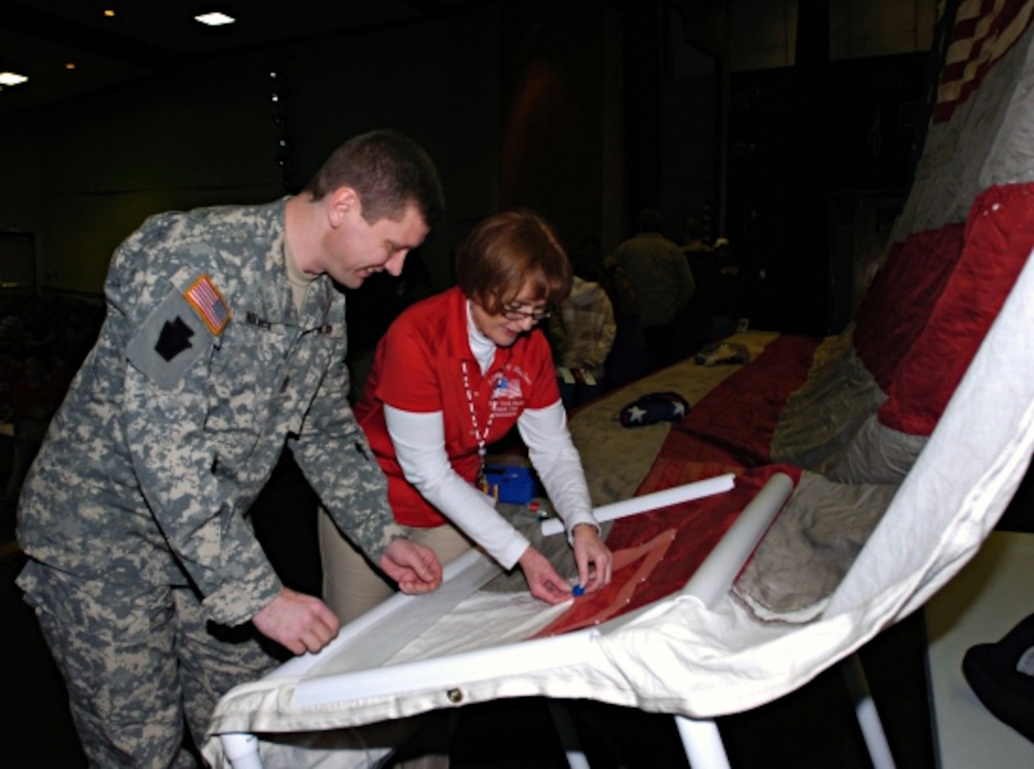 Army Command Sgt. Maj. George Holmes, a Pennsylvania Army National Guardmember, participates as one of 13 specially nominated “local heroes” in the National 9/11 Flag Tour stitching ceremony in Milford, Pa., Saturday, Feb. 12, 2011. Tour event manager Carolyn Deters (pictured) instructs visitors on the placing of their stitch in the traveling star-spangled banner, which once hung at the ground zero complex of the World Trade Center buildings and was severely damaged in the collapse of the towers.