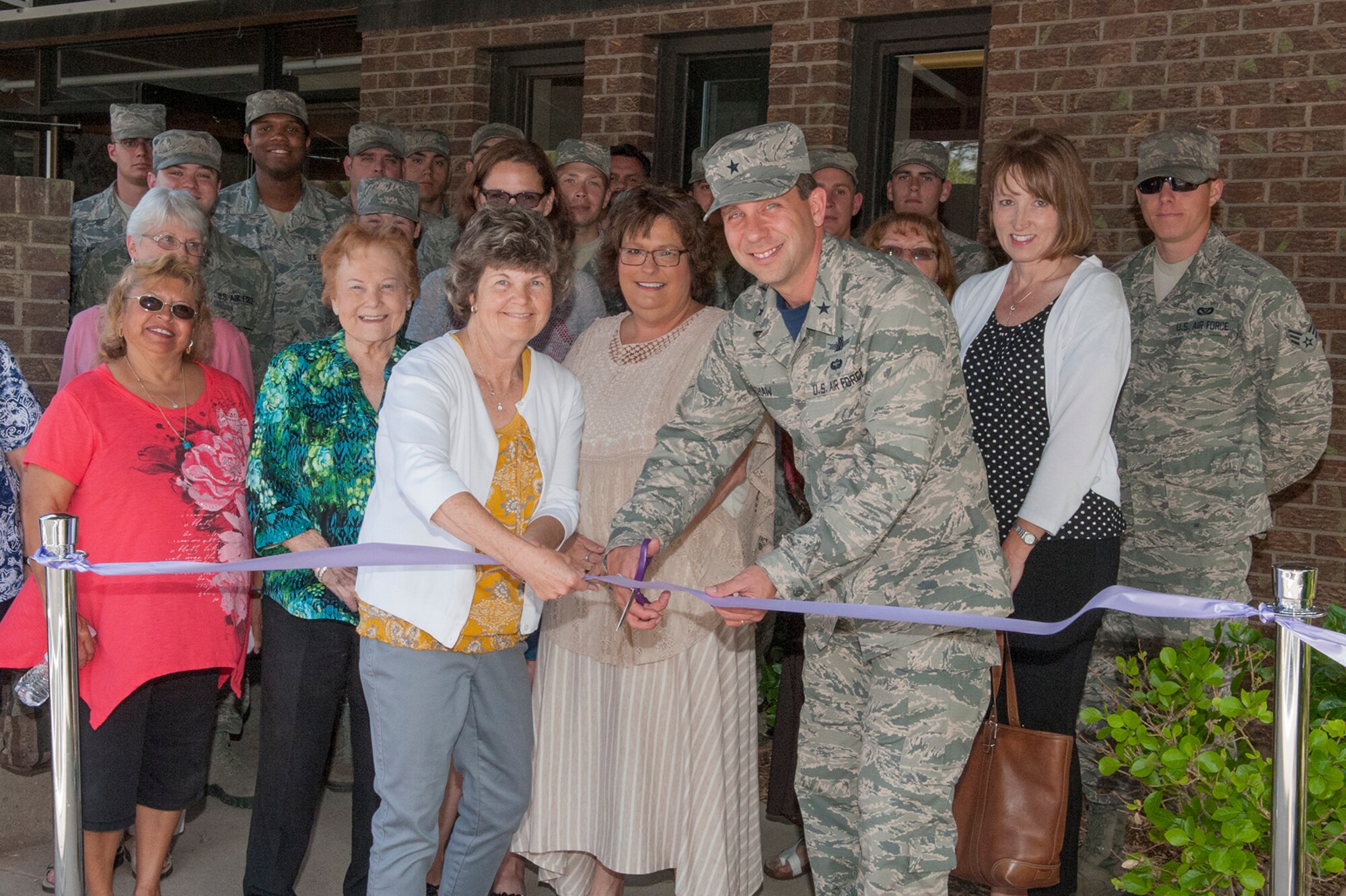 PETERSON AIR FORCE BASE, Colo. – (Left to right) Shelly Algeier (white sweater, yellow shirt), Thrift Shop manager, Rhonda Chozinski, president of the Peterson, Schriever, and Cheyenne Mountain Spouses’ Club, Brig. Gen. John Shaw, 21st Space Wing commander, and Tonia Shaw, Peterson Key Spouse, cut the ribbon at the shop’s new location in building 1525, across from the R.P. Lee Youth Center. Also joining in the ceremony are thrift shop volunteers and members of the 21st Civil Engineer Squadron, who helped renovate the new location. (U.S. Air Force photo by Philip Carter)