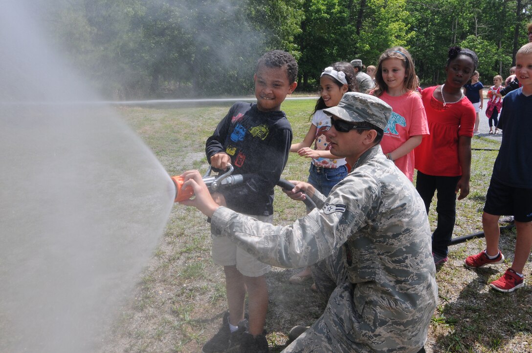 U.S. Air Force Airman 1st Class Scott Bramhall, from the New Jersey Air National Guard's 177th Fighter Wing Fire Department, helps a student use a fire hose on June 9, 2015 at Alder Avenue Middle School's Not All Heroes Wear Capes event in Egg Harbor Township, N.J. Local first responders and military personnel gathered at the school to provide a hands-on educational experience for students, teaching them about the services they provide to the local community. (U.S. Air National Guard photo by Airman 1st Class Amber Powell/Released)