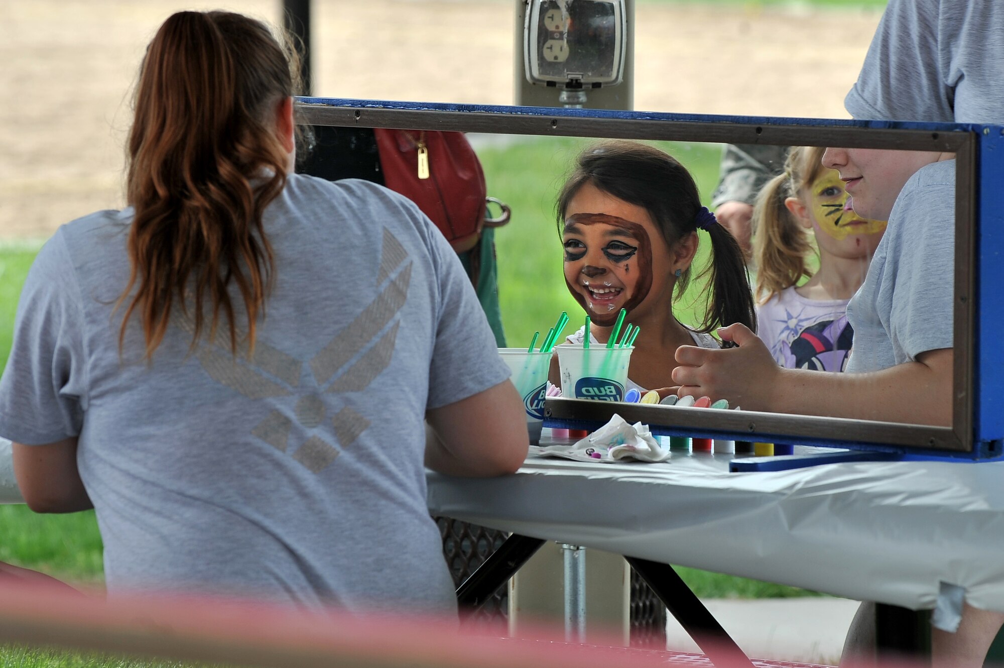 Six-year-old Lynnea, granddaughter of Civil Servant Perry Wilson, takes a glimpse of her face paint June 5 during the Offutt Appreciation Day Picnic held at the Offutt Base Lake. The picnic featured numerous inflatables, rock wall and several other children’s activities.  (U.S. Air Force photo by Josh Plueger/Released)