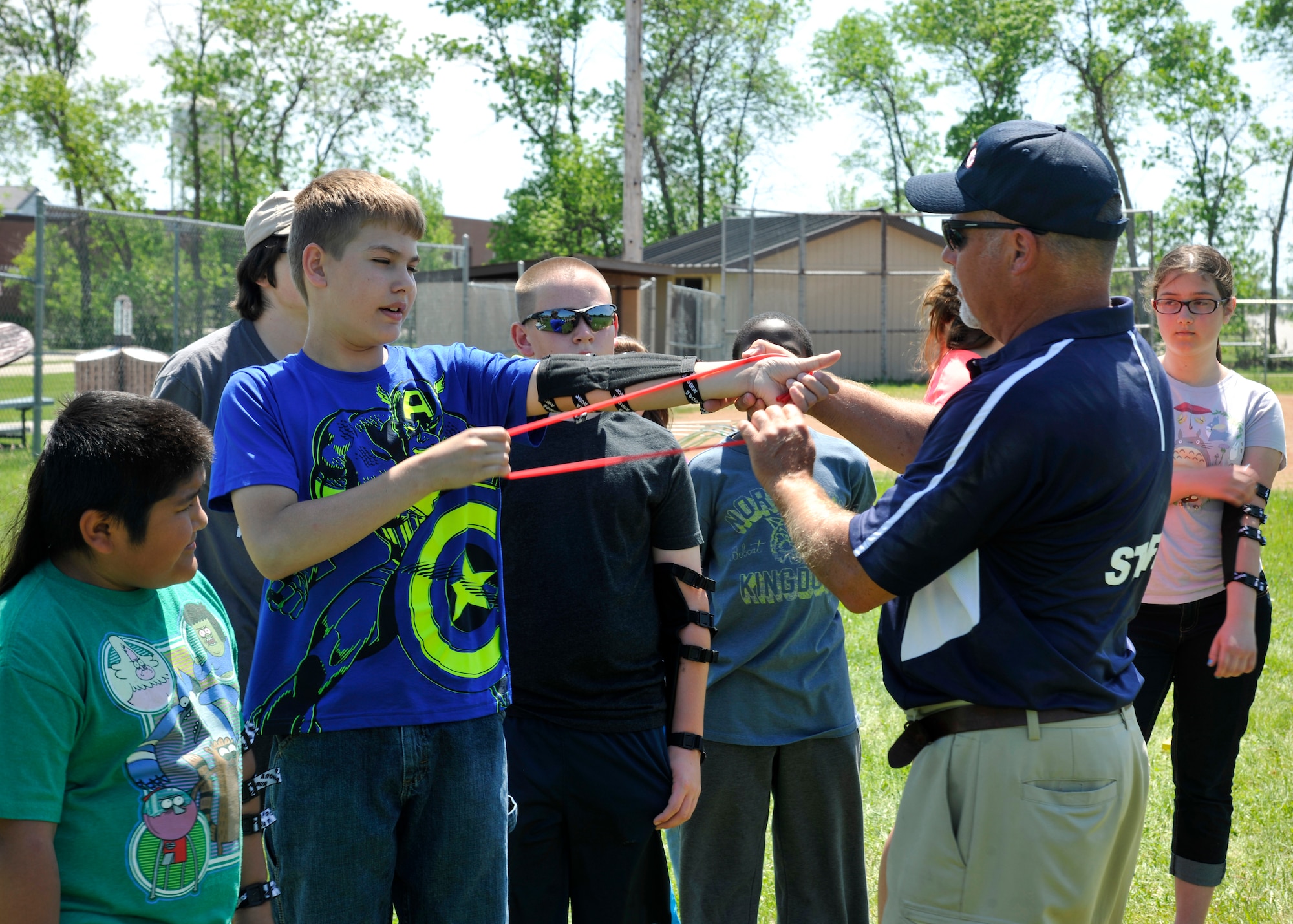 Mike Brown, archery instructor, teaches youth how to use a rubber stretch band during an archery camp June 9, 2015, on Grand Forks Air Force Base, N.D. The stretch band is an archery skill exercise to help students work on their release techniques and acts as a resistor on the bowstring to strength training exercises. (U.S. Air Force photo by Senior Airman Xavier Navarro/released)