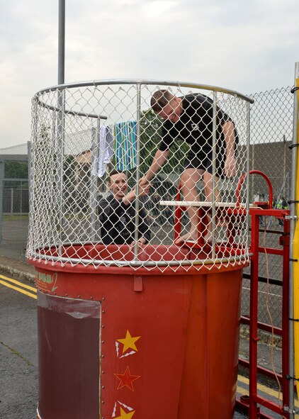 U.S. Air Force Col. Thomas D. Torkelson, right, 100th Air Refueling Wing commander, shakes the hand of the first Airman to hit a button and knock him into a dunk tank at the Unaccompanied Airmen's Appreciation Day event June 5, 2015, on RAF Mildenhall, England. The event was held to build morale of Airmen stationed here without families, and provided an opportunity for them to get together with base leadership and have fun. (U.S. Air Force photo by Karen Abeyasekere/Released)