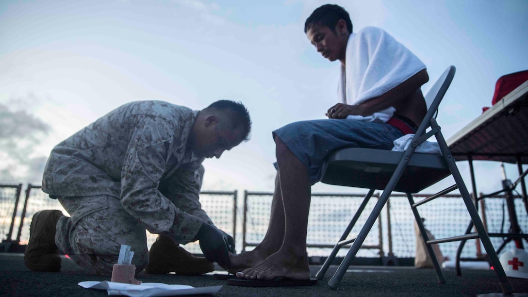 U.S. Navy Petty Officer 3rd Class Guillermo Lopez, with Combat Logistics Battalion 15, 15th Marine Expeditionary Unit, provides medical attention to a distressed mariner aboard the USS Rushmore (LSD 47) at sea in the Pacific Ocean, June 10, 2015. Rushmore rendered assistance to the distressed mariners in the waters between the Indonesian islands of Kalimantan and Sulawesi. Once on board, evacuees were provided food and medical attention by Marines and sailors of the 15th Marine Expeditionary Unit and Essex Amphibious Ready Group. 