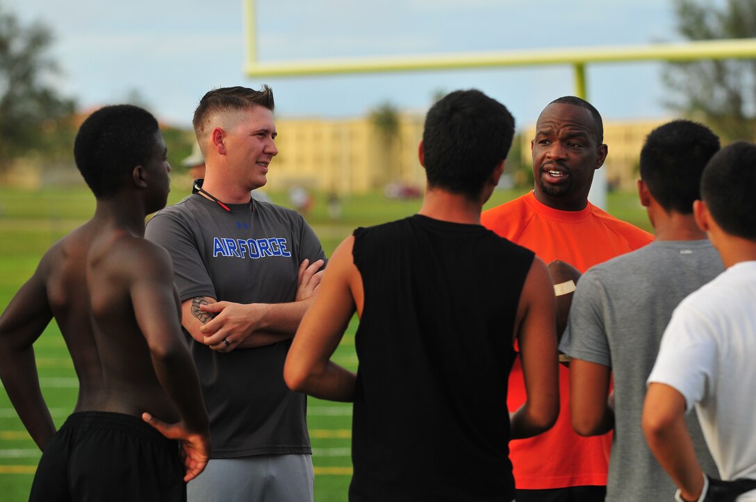 Senior Airman Presley Griffith, center left, listens as Jacob Dowdell, Guam High School head coach, center right, gives feedback to high school athletes June 2, 2015, at Andersen Air Force Base, Guam. Griffith, 36th Mobility Response Squadron executive assistant, created a free spring practice camp to offer local high school athletes an additional mentoring and practice opportunity before football season begins and to share his passion for football. (U.S. Air Force photo by Senior Airman Alexander W. Riedel/Released)