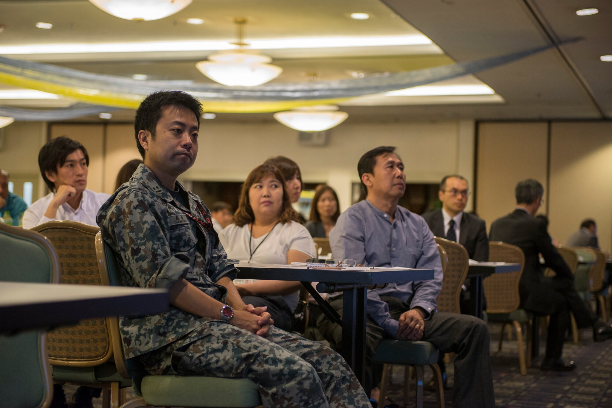 A Japan Self-Defense Force member and representatives from local businesses listen to a speech given during a Vendor Fair event at Yokota Air Base, Japan, June 10, 2015. The fair was hosted by the 374th Contracting Squadron to inform local businesses of opportunities to work with the U.S. government and put money back into the local community. (U.S. Air Force photo by Staff Sgt. Cody H. Ramirez/Released)