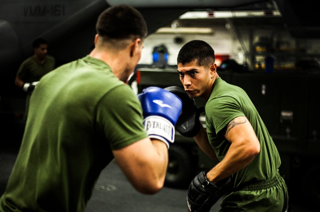 U.S. Marine Cpl. Roman Fernandez, right, instructs a Marine on punching techniques in the hangar bay of the USS Essex (LHD 2) in the Philippine Sea, June 2, 2015. Fernandez is a team leader with Lima Company, Battalion Landing Team 3rd Battalion, 1st Marine Regiment, 15th Marine Expeditionary Unit. The Marines are learning boxing techniques to improve their mental and physical well-being during their seven-month deployment. (U.S. Marine Corps photo by Cpl. Elize McKelvey/Released)