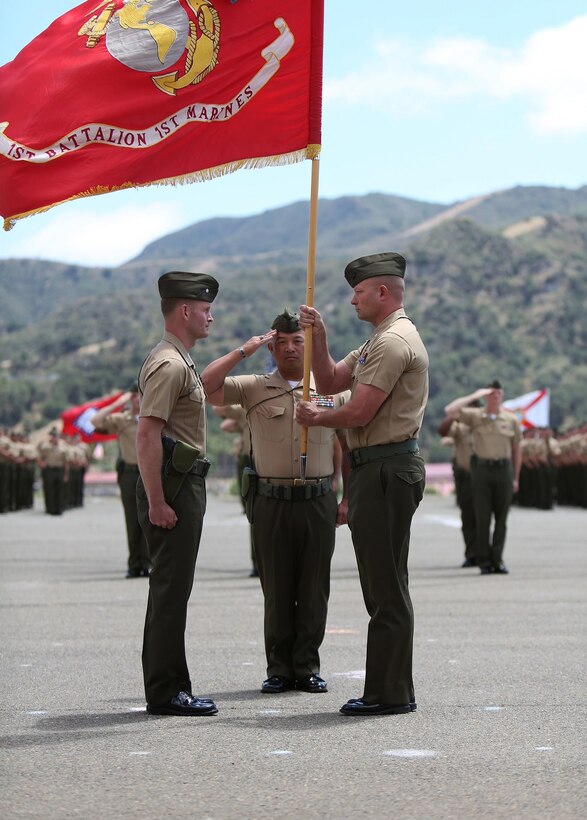 Lieutenant Col. Lance A. Jackola, battalion commander of 1st Battalion, 1st Marine Regiment, 1st Marine Division, formally relinquishes his command by handing the battalion colors to his successor Lt. Col. Steven M. Sutey. Sutey has several past deployments with the 1st Marine Division and said he is proud to command and serve once again with the unit. (U.S. Marine Corps photo by Cpl. Carson A. Gramley/Released)
