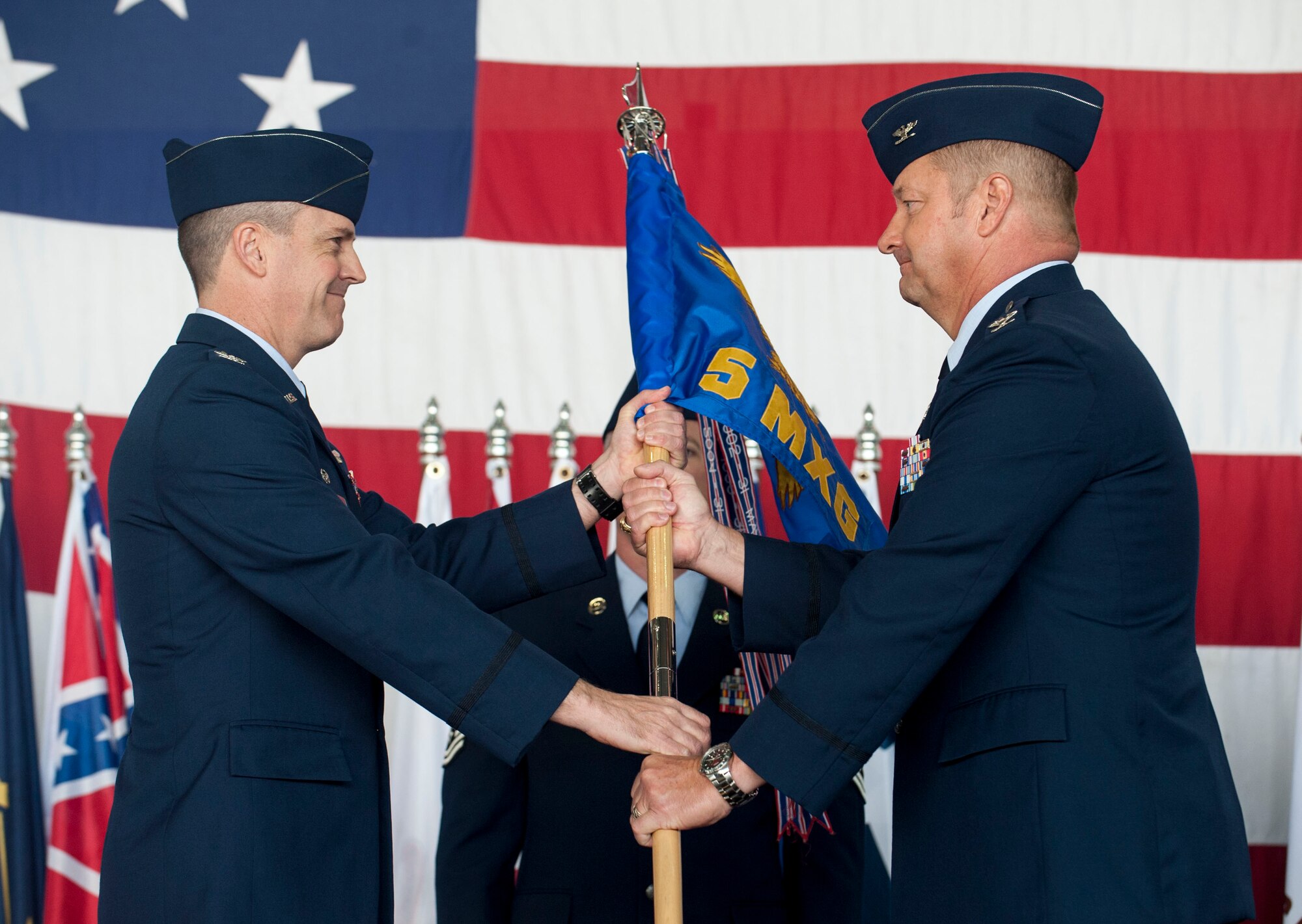 Col. Jason Armagost, 5th Bomb Wing commander (left), hands the guidon for the 5th Maintenance Group to its new commander Col. Thomas Kirkham (right), at Minot Air Force Base, N.D., June 12, 2015. During the ceremony Kirkham expressed enthusiasm at beginning work as the 5th MSG’s commander and leading them to future success. (U.S. Air Force photo/Senior Airman Stephanie Morris)