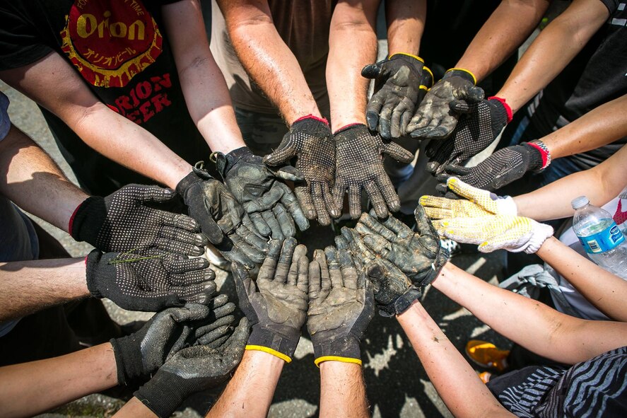 Okinawa Outreach volunteers display their muddy gloves following a two-hour clean-up session May 30, 2015, at Care-house Hibiscus in Okinawa City, Japan. Okinawa Outreach, a committee belonging to Kadena Air Base's Top 3 organization, was formed to provide opportunities for Team Kadena involvement in the Okinawan community. (Courtesy photo by Master Sgt. Steven Whitley)