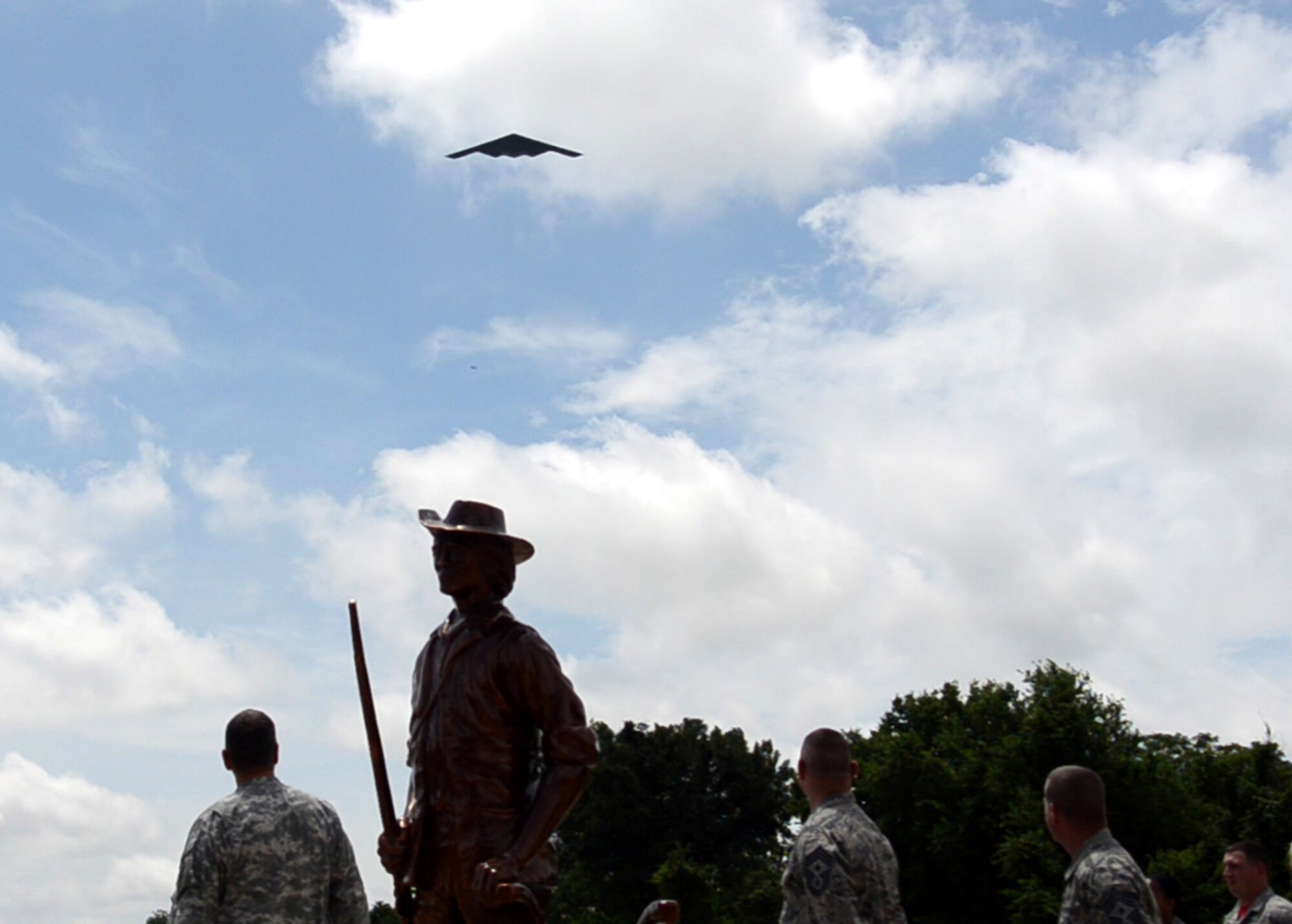 The B-2 Spirit stealth bomber flies overhead the newly-dedicated 131st Bomb Wing Heritage Park as Maj. Gen. Steve Danner, adjutant general of Missouri, Chief Master Sgt. Paul Joseph Sluder, Missouri Air National Guard command chief, and Chief Master Sgt. Paul Carney, 131st Bomb Wing command chief, look on at Whiteman Air Force Base, Mo., June 12, 2015.  The ceremony dedicated three jets that have been a part of the 131st culture and are now a permanent part of Whiteman.  