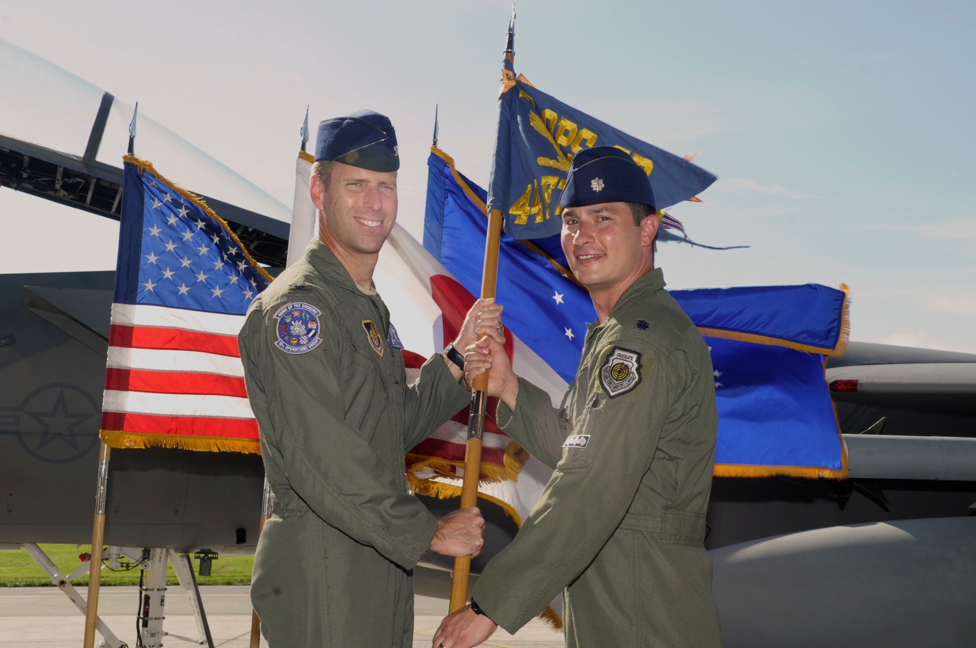 U.S. Air Force Col. David A. Mineau, 18th Operations Group commander, passes the 44th Fighter Squadron guidon to Lt. Col. Kevin Jamieson as he takes command of the 44th FS during a ceremony on Kadena Air Base, Japan, June 11, 2015. During the ceremony, Lt. Col. Michael Rowe relinquished command of the squadron after leading it for nearly two years. (U.S. Air Force photo by Airman 1st Class Zackary A. Henry/Released)