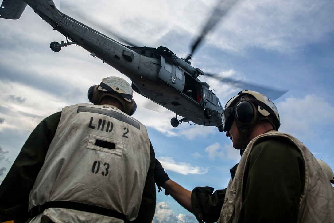 U.S. Marines with the 15th Marine Expeditionary Unit watch an MH-60S Sea Hawk take off to pick up more supplies for the USS Essex (LHD 2) during a replenishment-at-sea in the South China Sea, June 14, 2015. These combat cargo Marines helped transport mail and supplies from the flight deck to the rest of the ship as the USS Essex transitions to their 5th Fleet area of responsibility. (U.S. Marine Corps photo by Cpl. Anna Albrecht/Released)