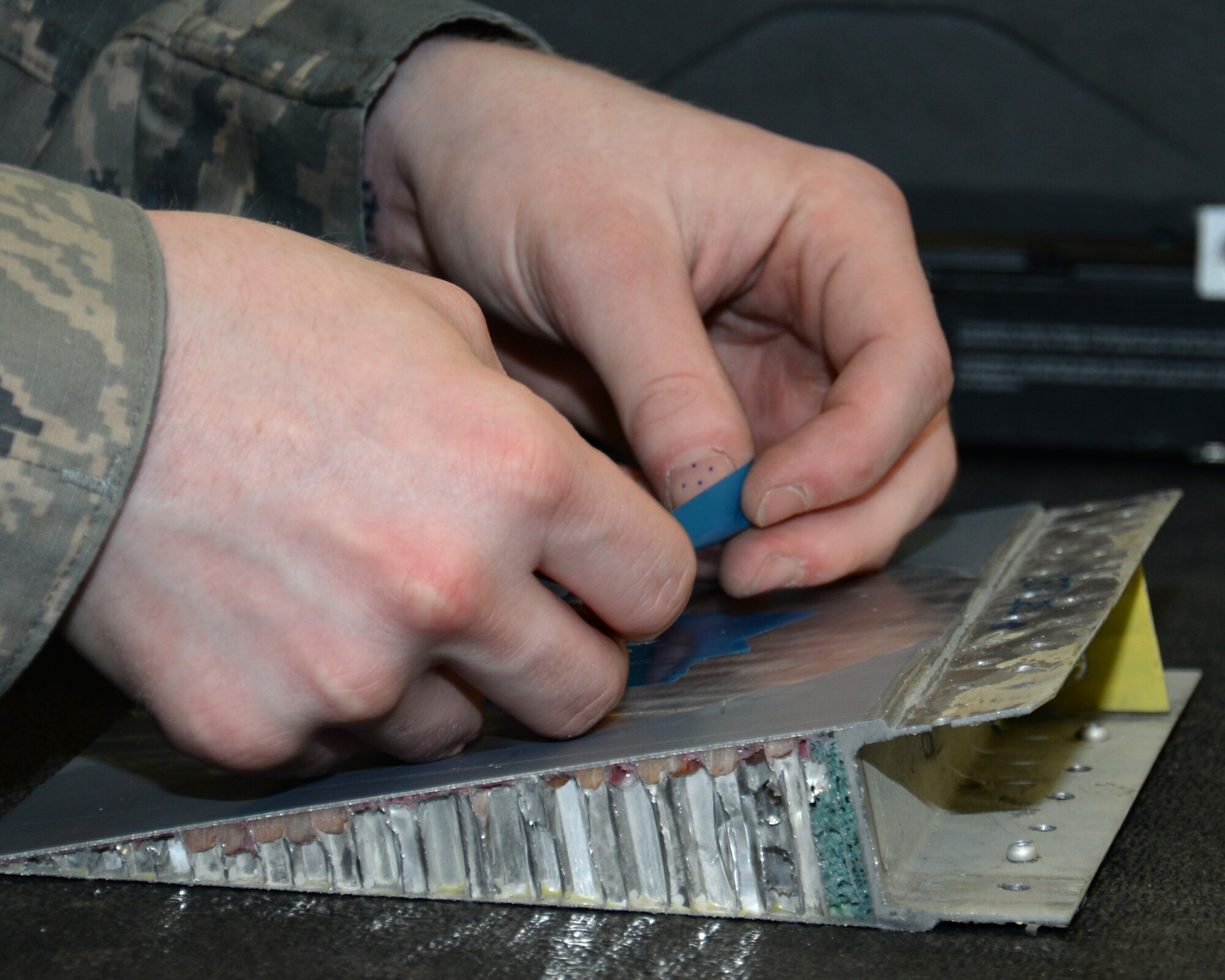 U.S. Air Force Airman 1st Class Donavan Jerles, 100th Maintenance Squadron Aircraft Structural apprentice from Gulf Shores, Ala., places tape on a honeycomb core preparing the surface for fiberglass repair June 3, 2015, on RAF Mildenhall, England. The honeycomb core is used to distribute the load stress across the entirety of the panel. The tape was placed on the surface to stop any excess adhesive from bonding to the surface metal. (U.S. Air Force photo by Gina Randall/Released)