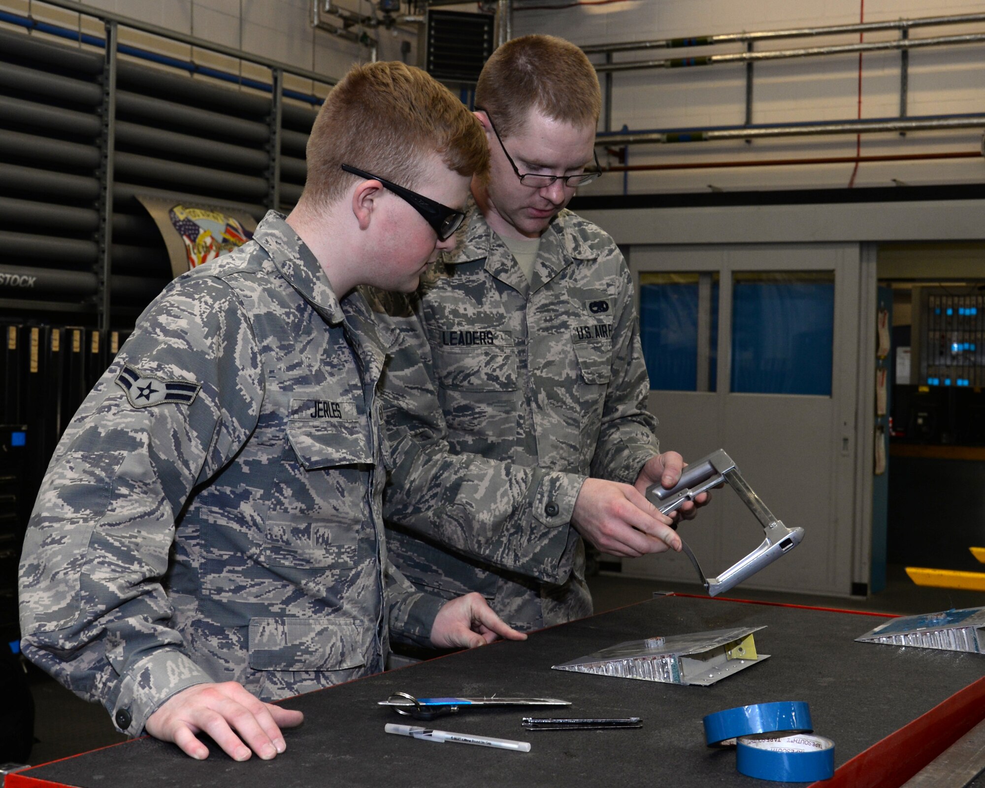 U.S. Air Force Airman 1st Class Cody Leaders, right, 100th Maintenance Squadron Aircraft Structural Maintenance technician from Elizabeth, Colo., shows U.S. Air Force Airman 1st Class Donavan Jerles, left, 100th MXS Aircraft Structural apprentice from Gulf Shores, Ala., how to adjust a saw June 3, 2015, on RAF Mildenhall, England. The hack saw is placed in the holder to create tension on the blade so it doesn’t bow. The Airman used the saw to cut the core straight and level with the surface of the panel. (U.S. Air Force photo by Gina Randall/Released)